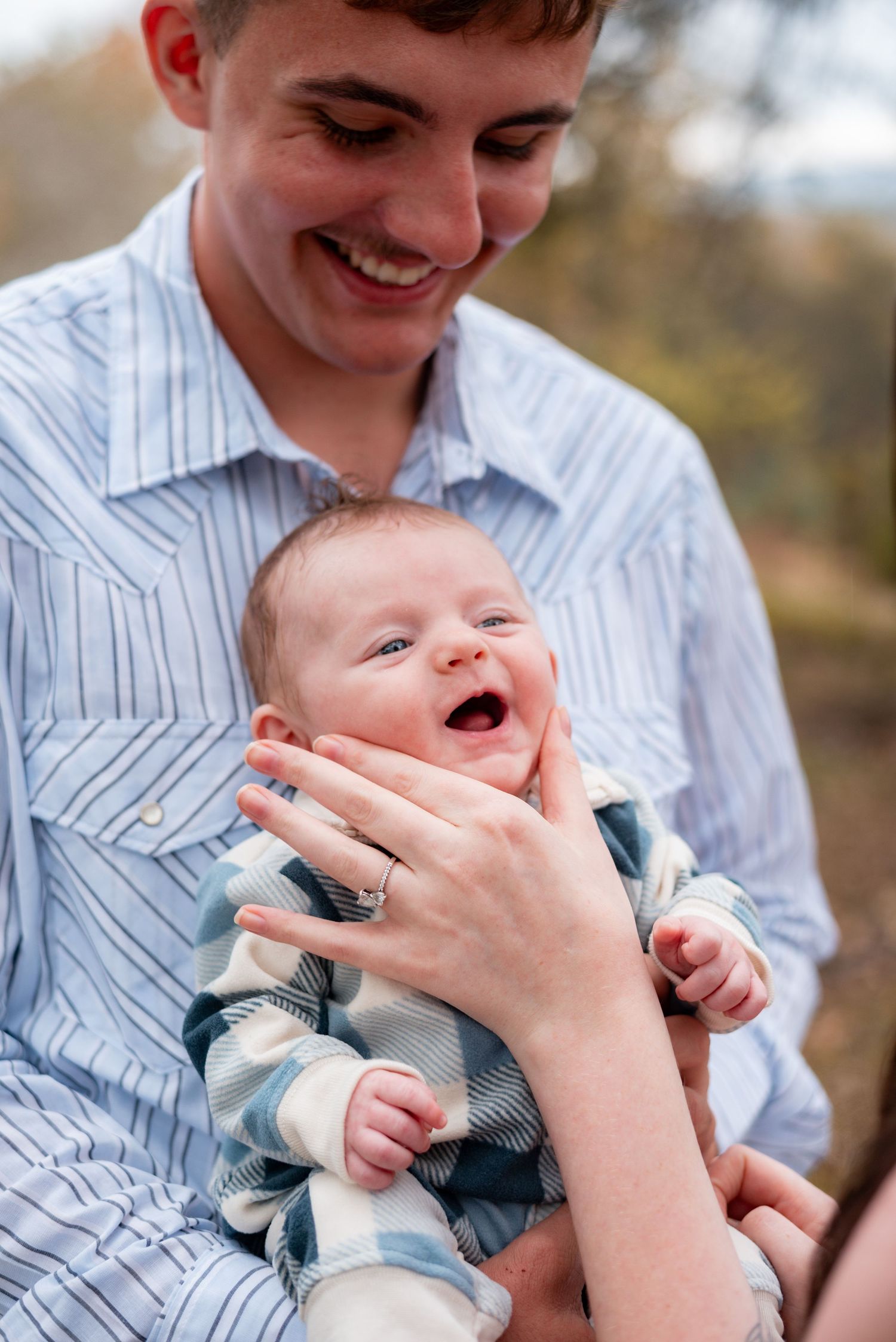 Tender moment between parent and infant in blue plaid vest and white striped shirt.
