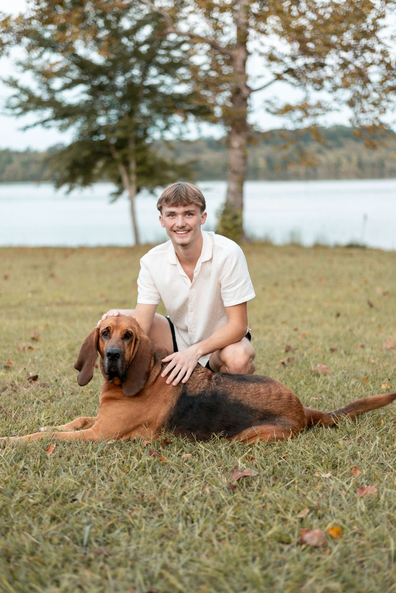 Person in white shirt lies in grass with brown dog during outdoor photo session.