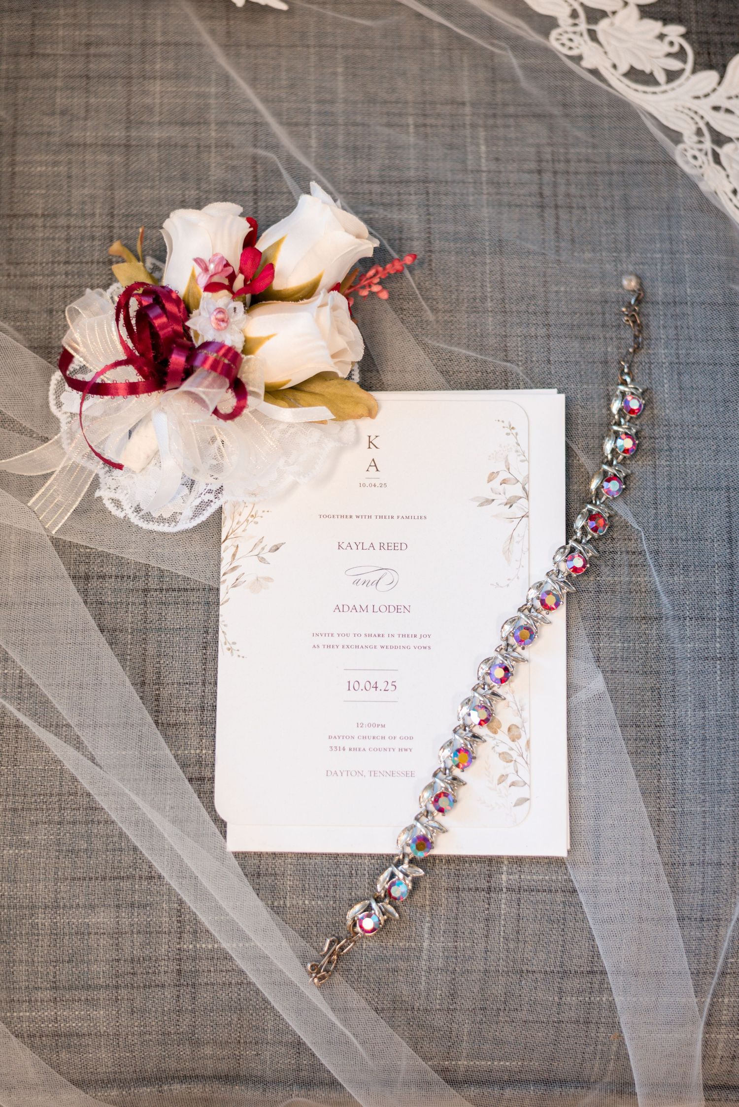 Wedding invitation with floral arrangement and crystal jewelry on gray textile background.