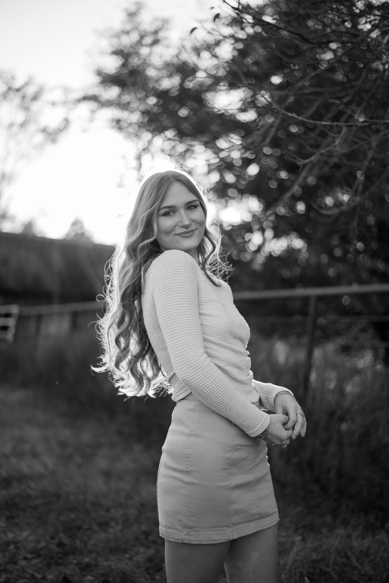 Portrait of someone in a cream sweater posing against a natural outdoor background at sunset.
