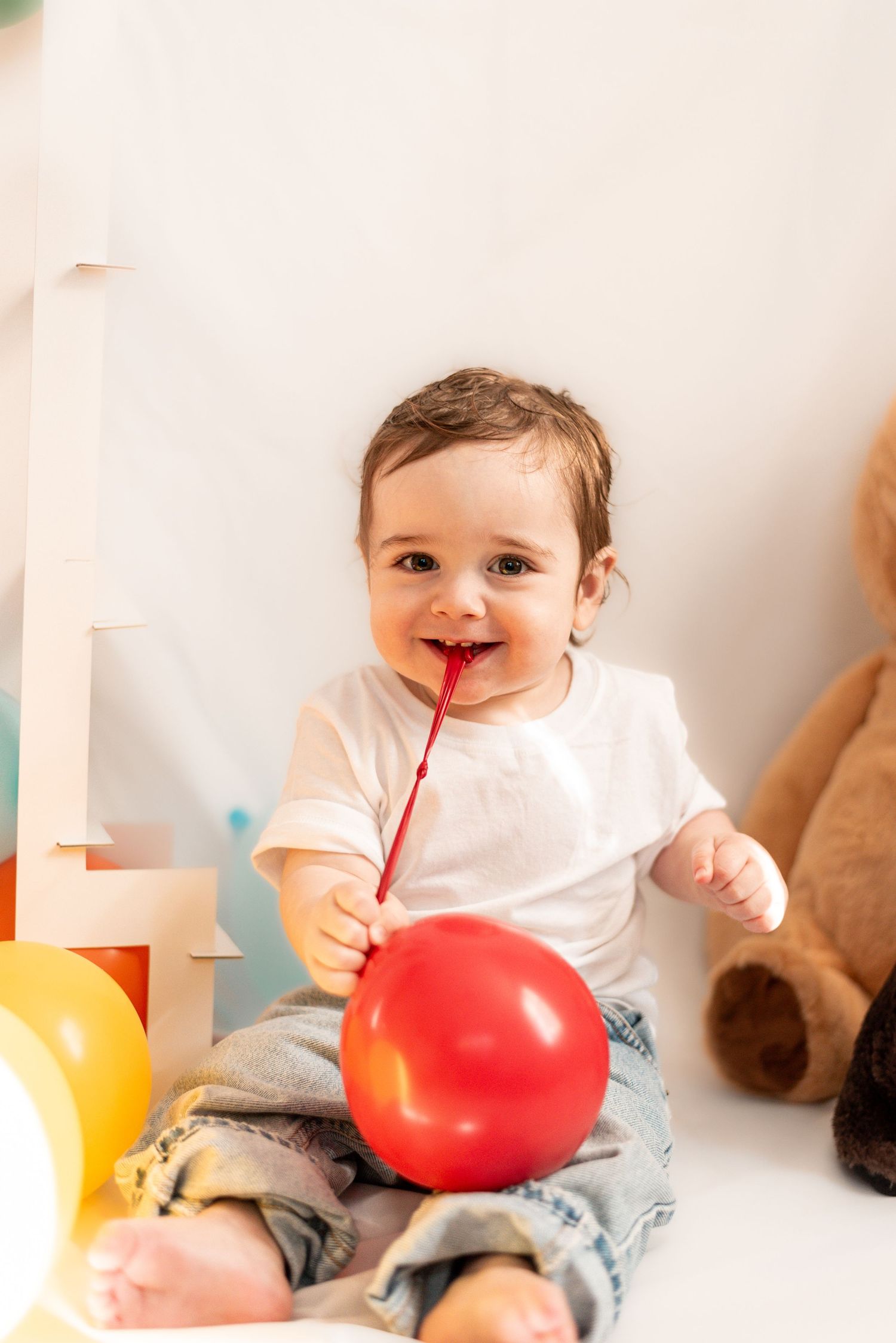A toddler plays with a red balloon while sitting on the floor.
