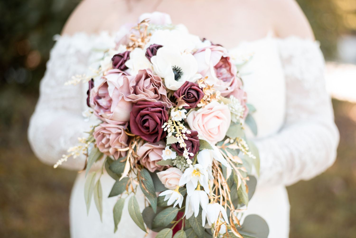 Wedding bouquet featuring burgundy and pink roses with cascading eucalyptus leaves.