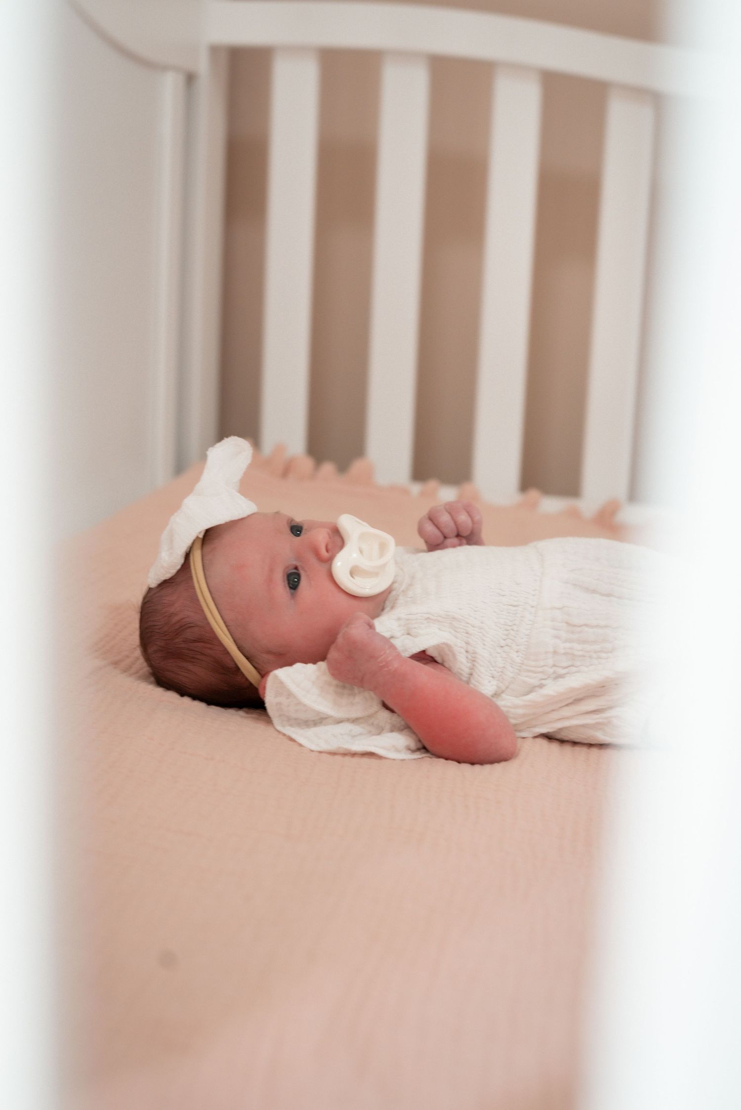 Newborn resting in white crib wearing soft white outfit with medical monitors.