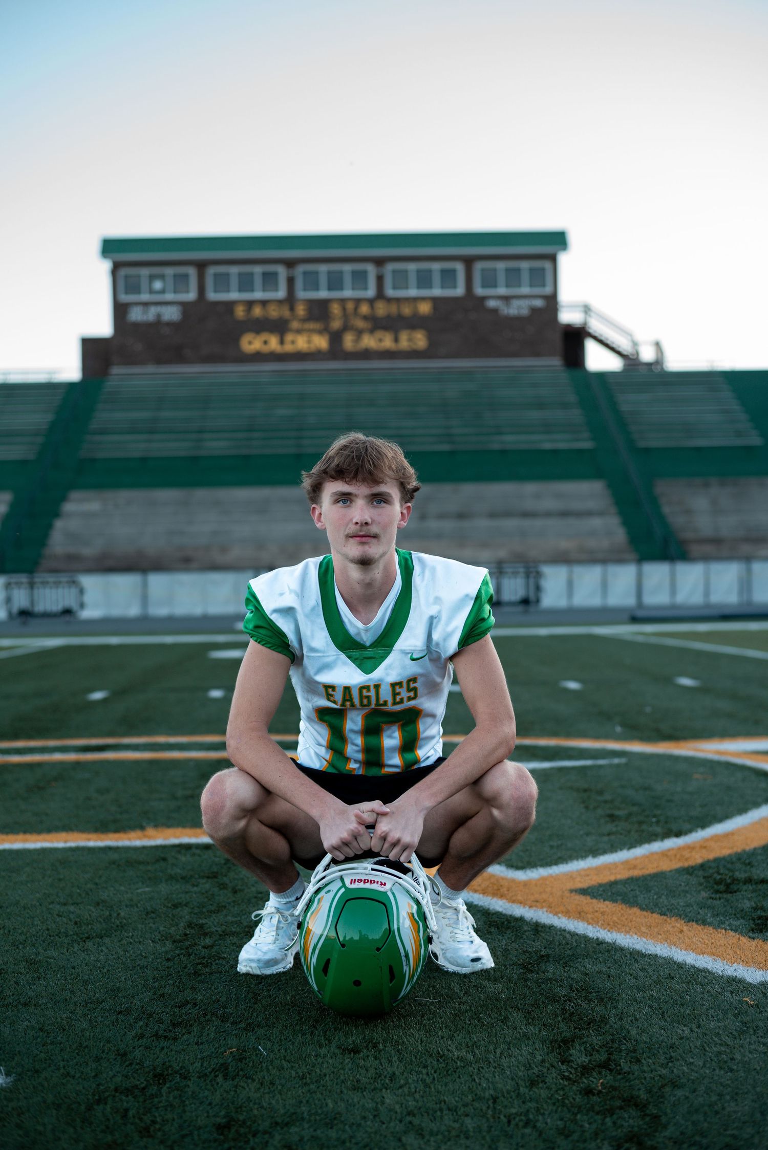 Football player in green and white uniform poses with ball on field at Eagles stadium.