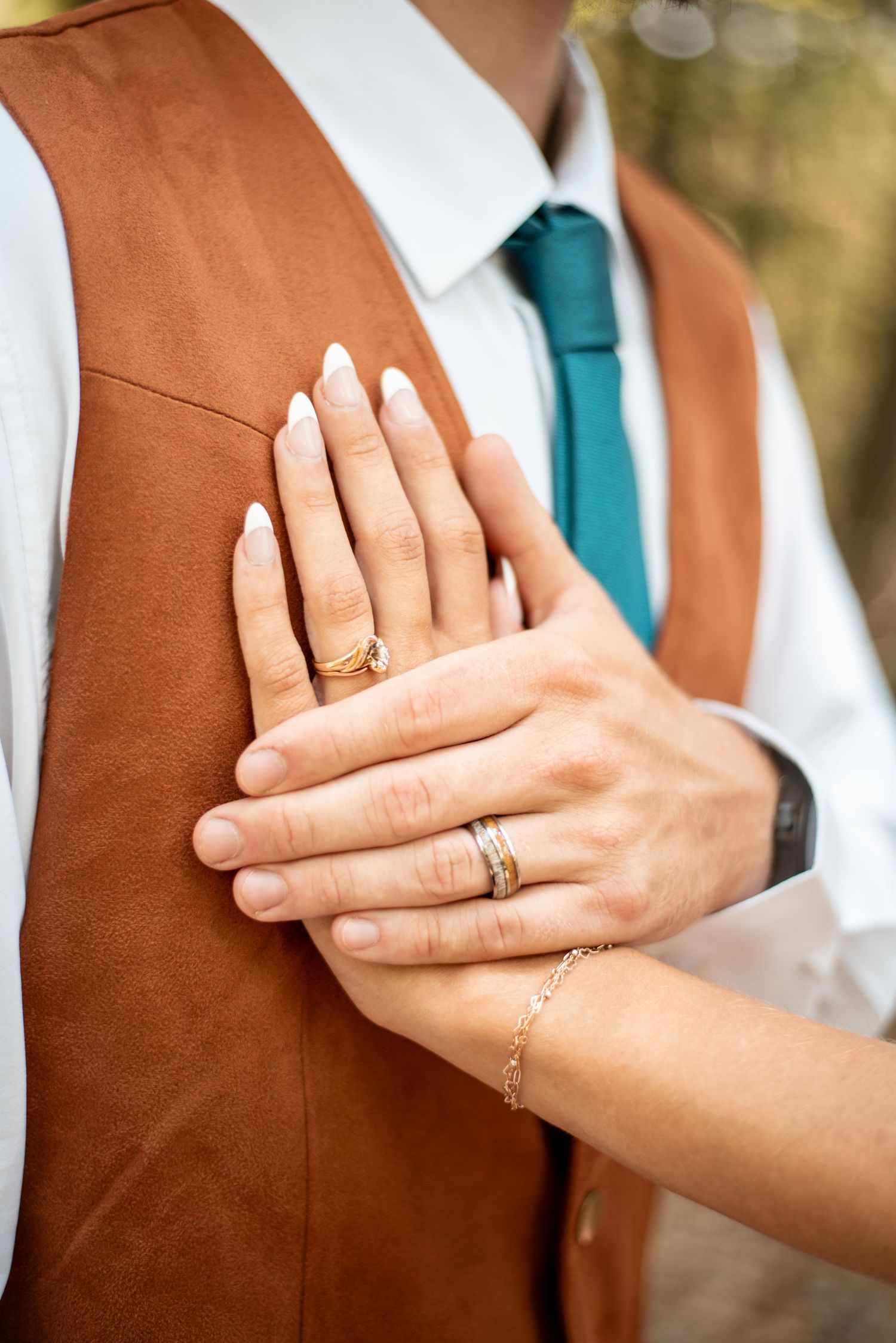Close-up shots of hands with wedding rings against a brown vest.