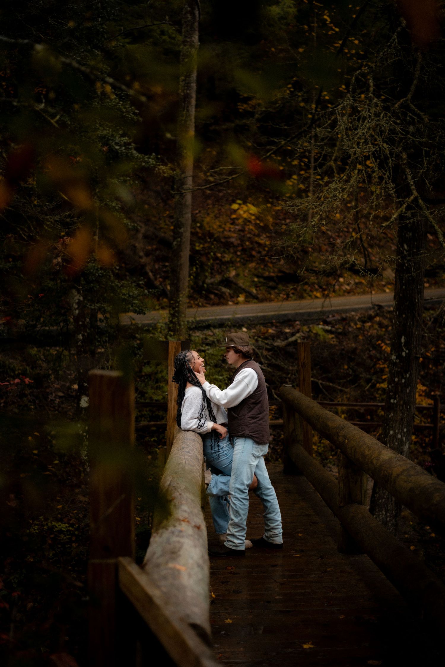 A couple shares an intimate moment on wooden steps surrounded by autumn foliage.
