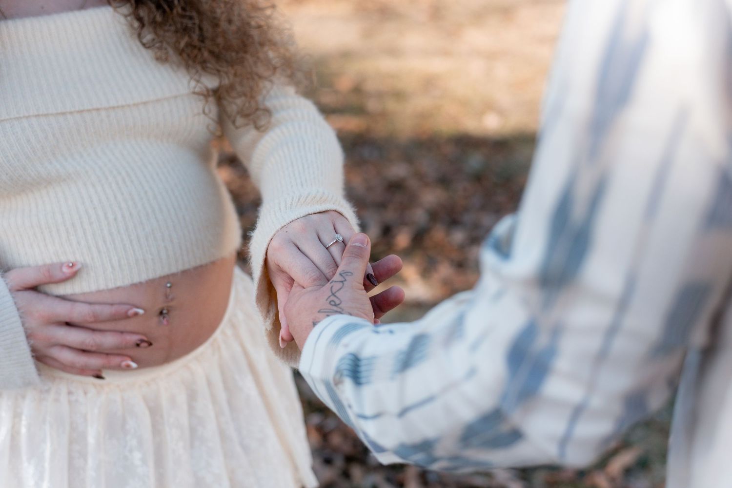 Side view of pregnant woman's belly with hands cradling bump outdoors.