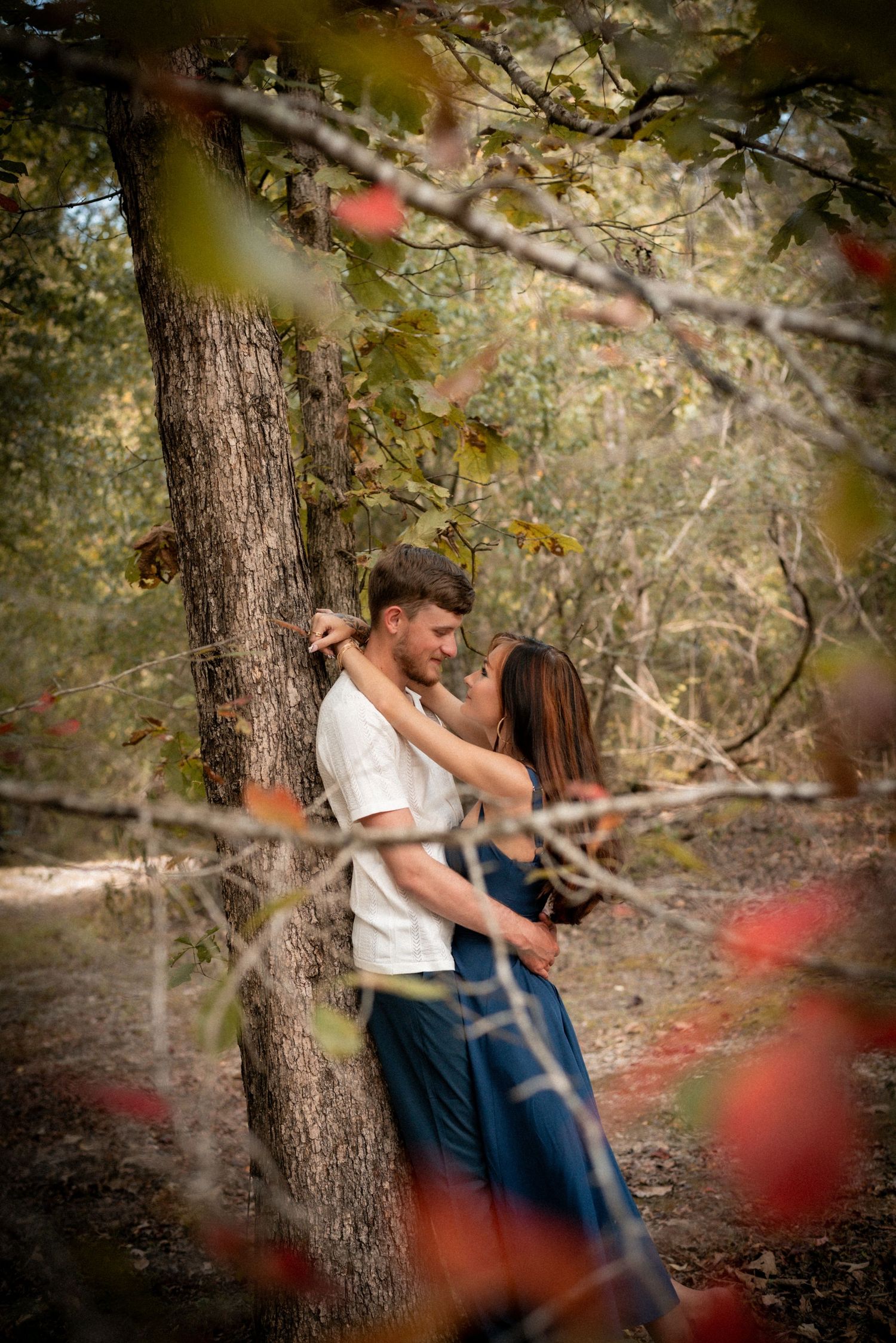 A romantic couple embraces among fall foliage and tree trunks in a forest.