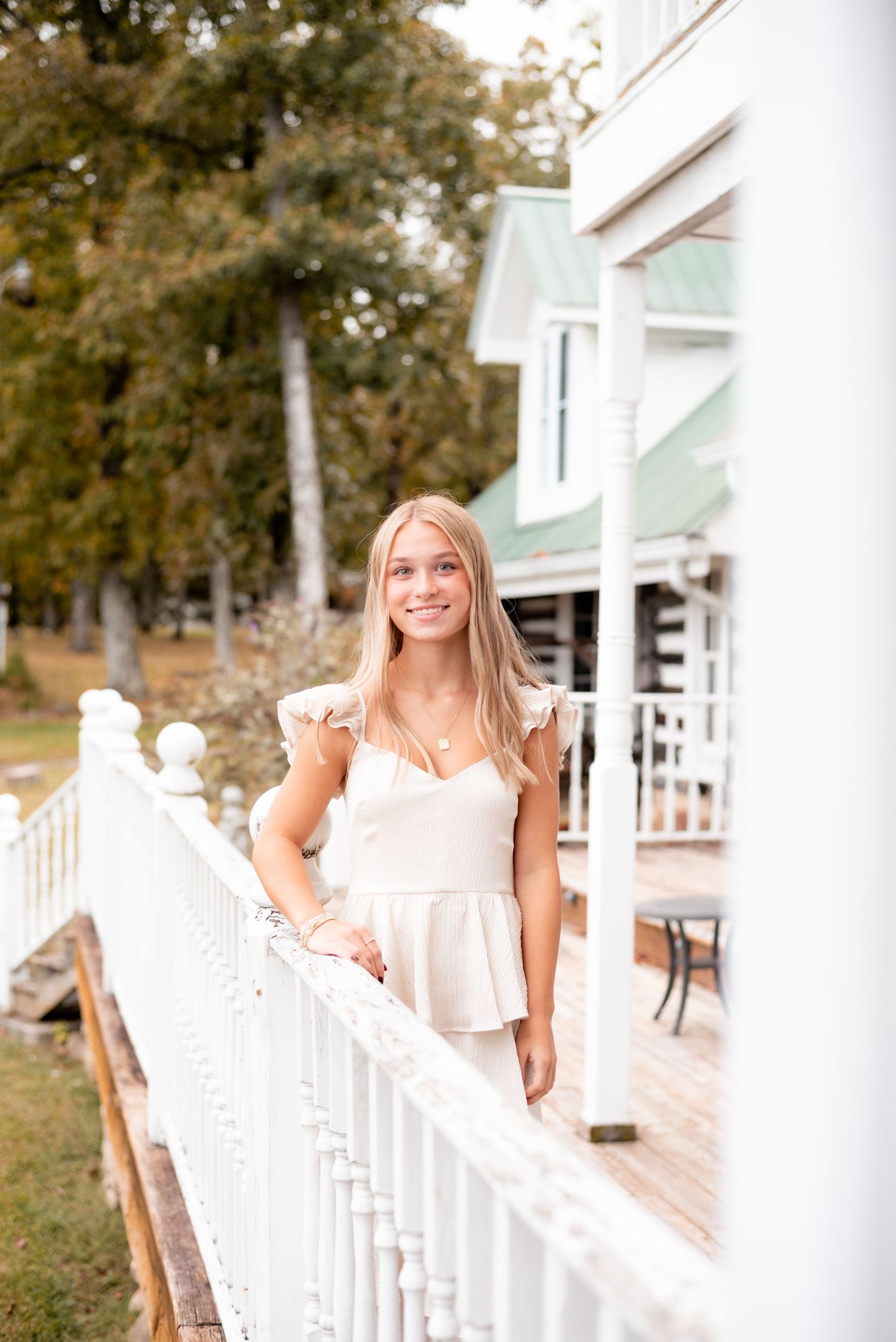 Cheerful portrait on white porch railing wearing cream colored ruffle dress.