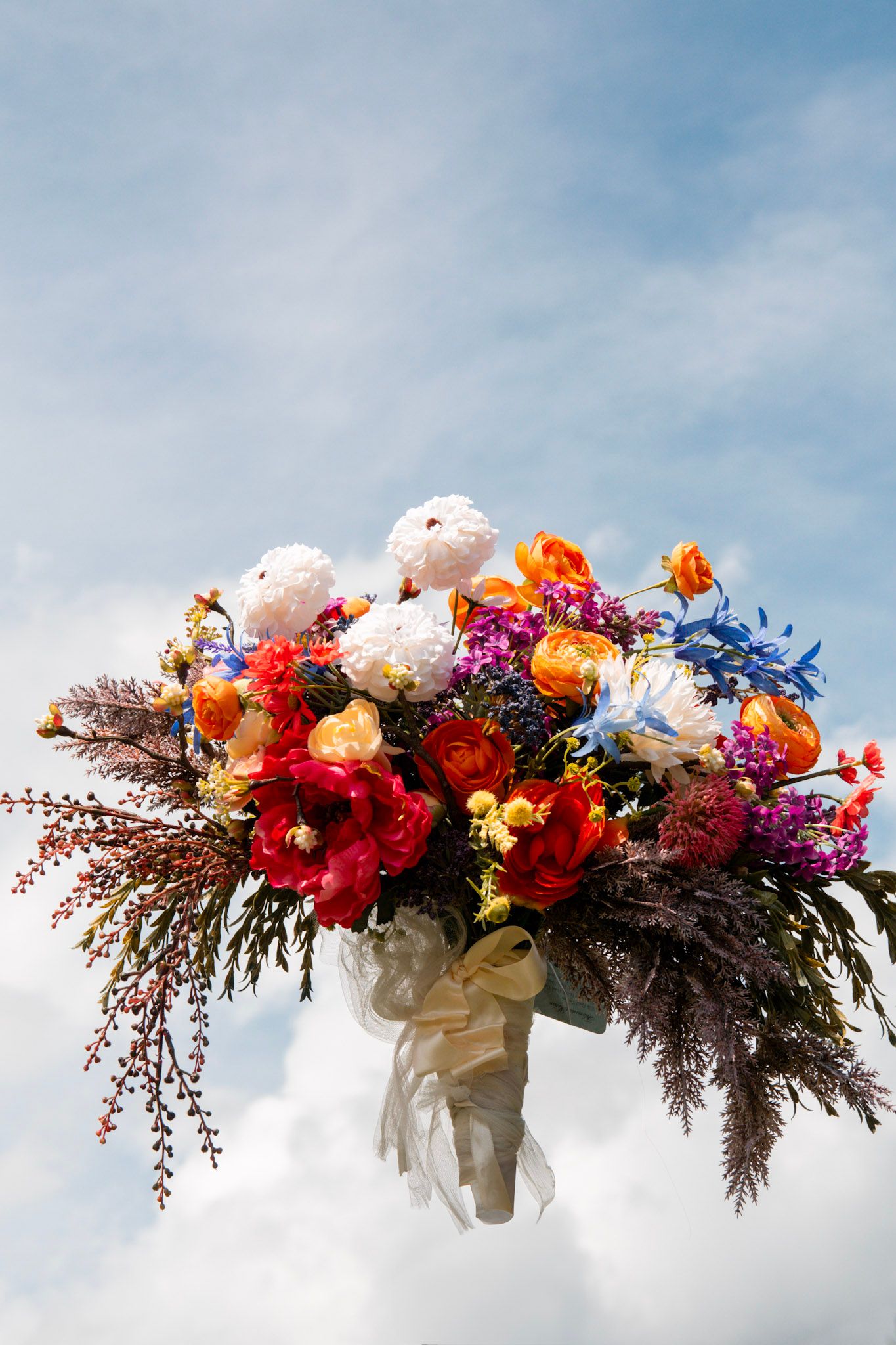 Colorful floral arch arrangement against blue sky with vibrant red and pink blooms.