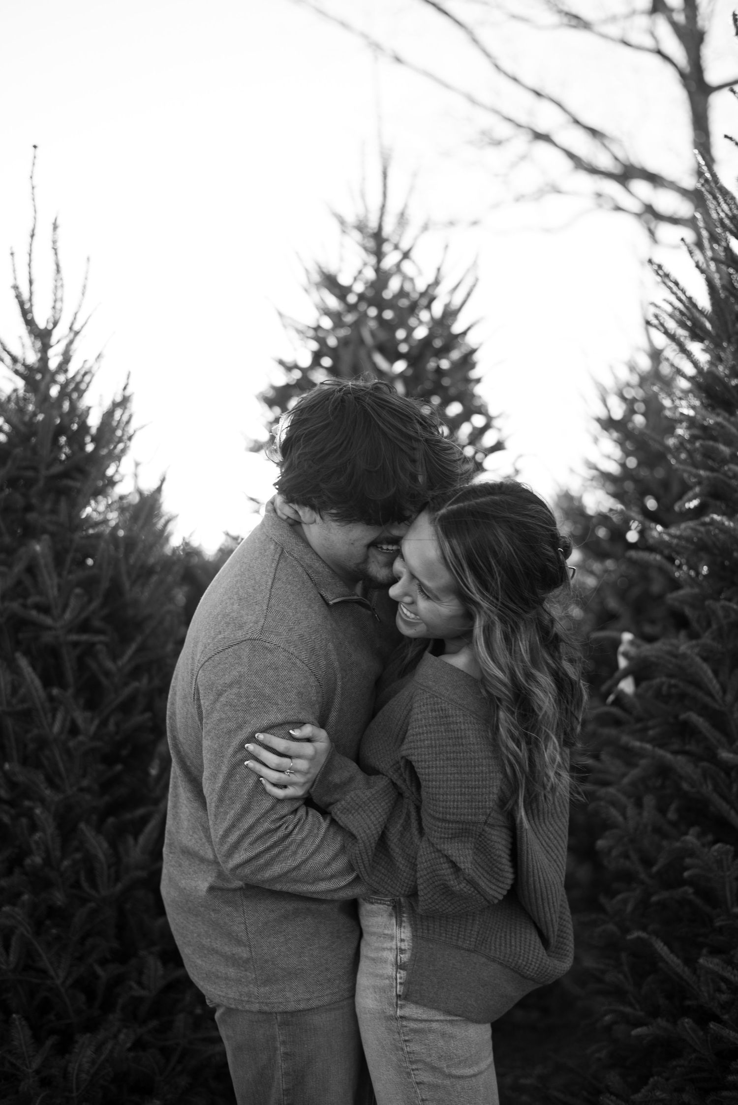 Intimate black and white portrait of couple embracing among evergreen trees.