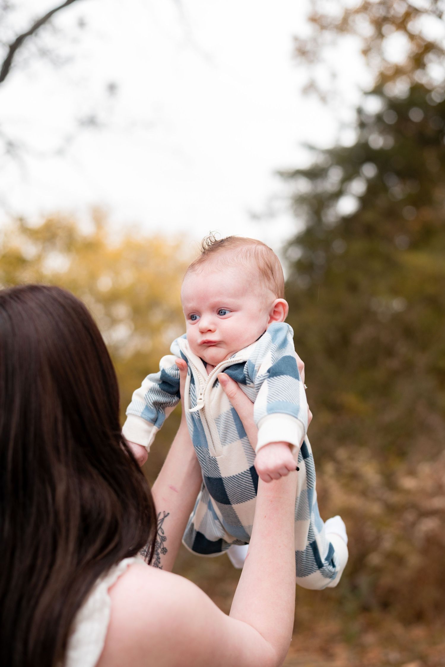 Baby in blue and white outfit being lifted in outdoor setting.