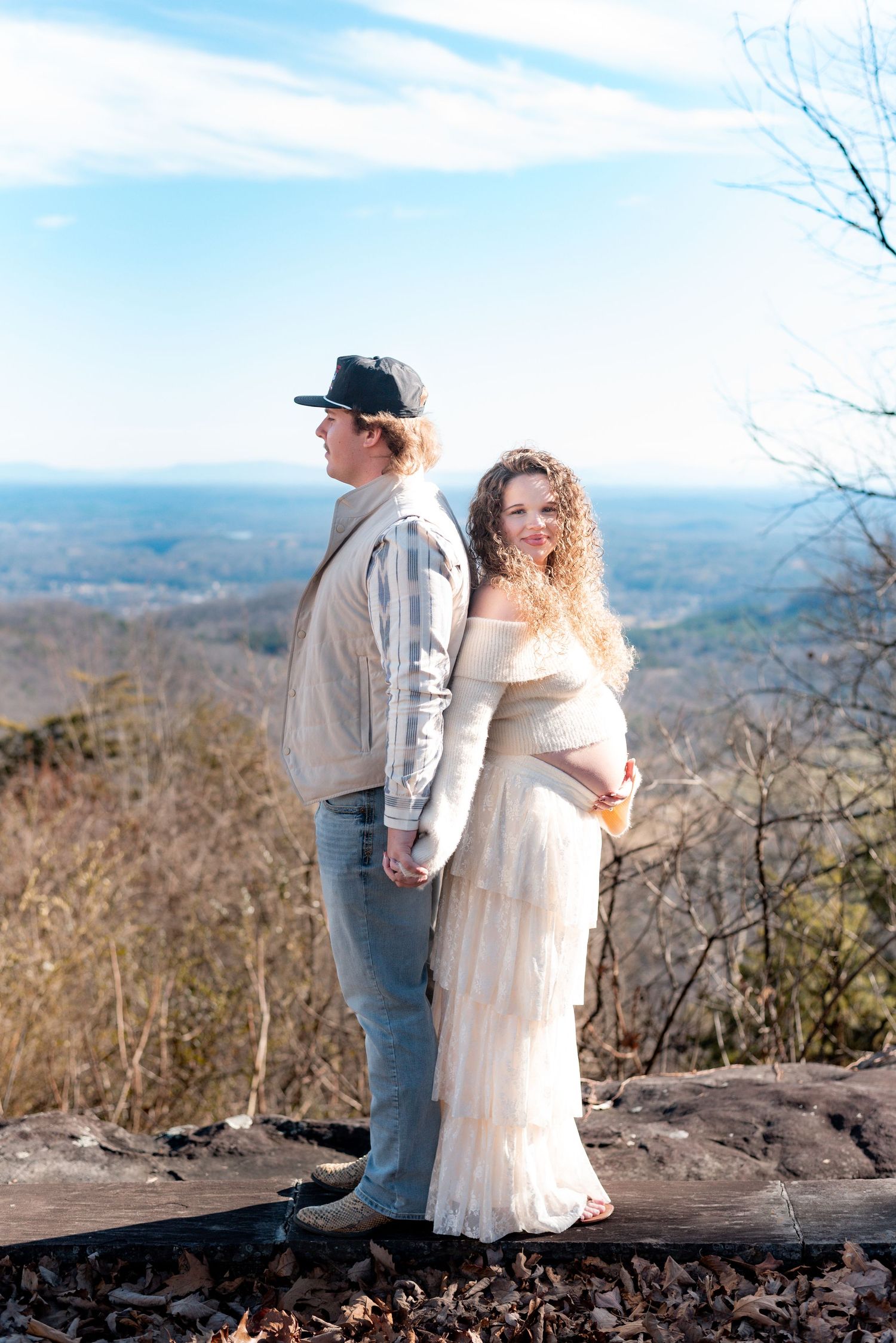 Maternity couple poses on mountain overlook with scenic valley view.