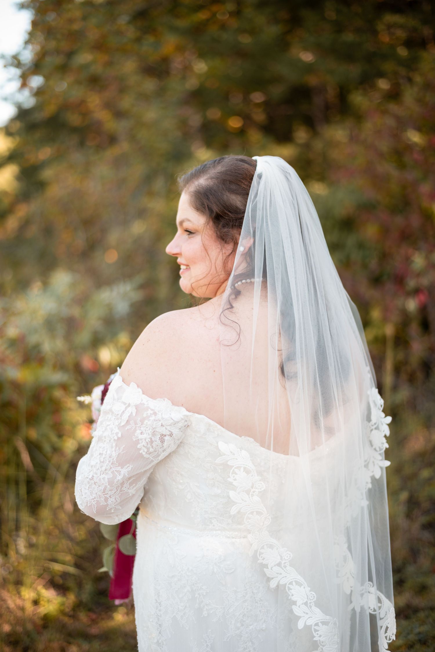 Back view of bride in lace dress with delicate veil against autumn background.