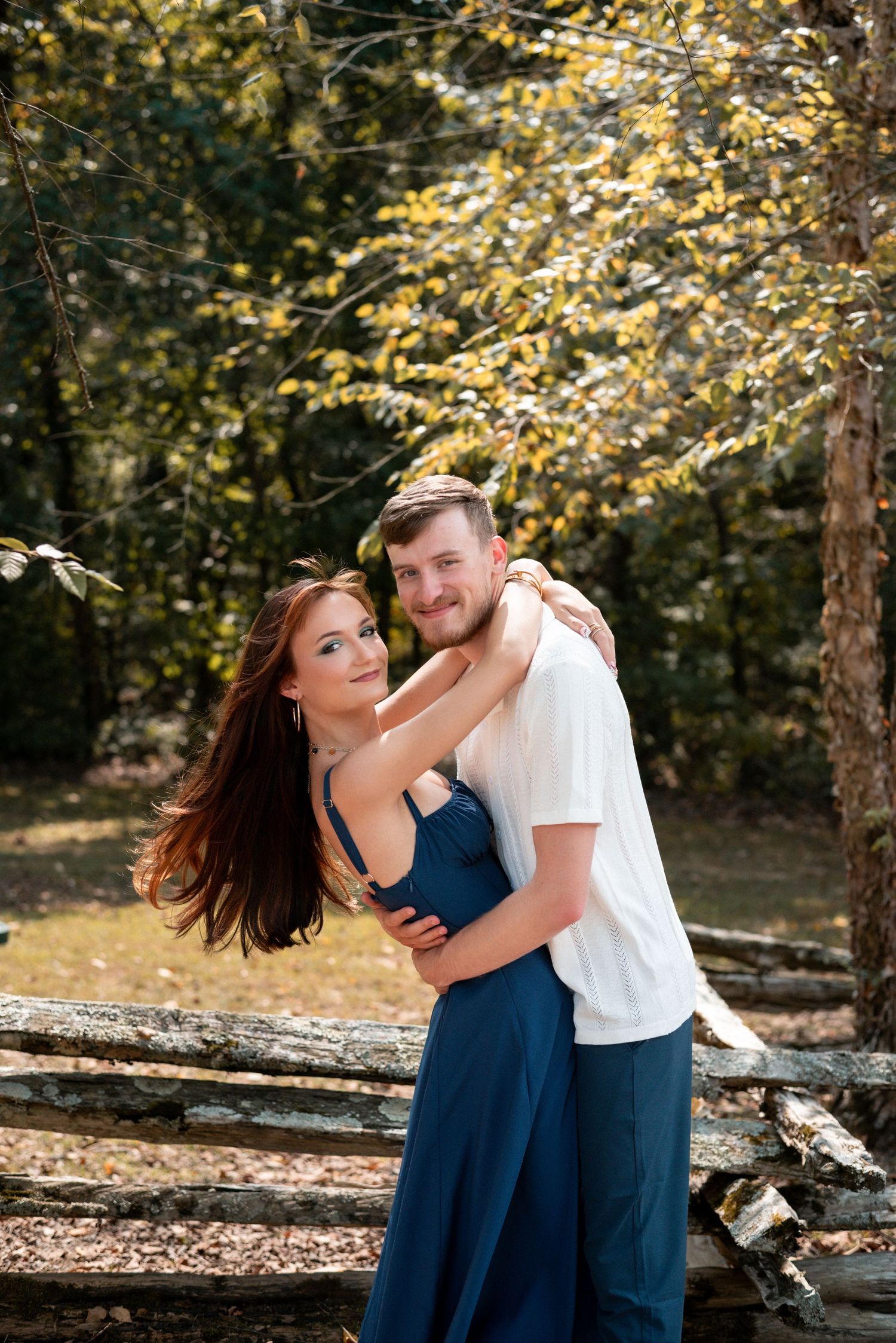 A playful couple shares laughter while posing together in an autumn forest setting.