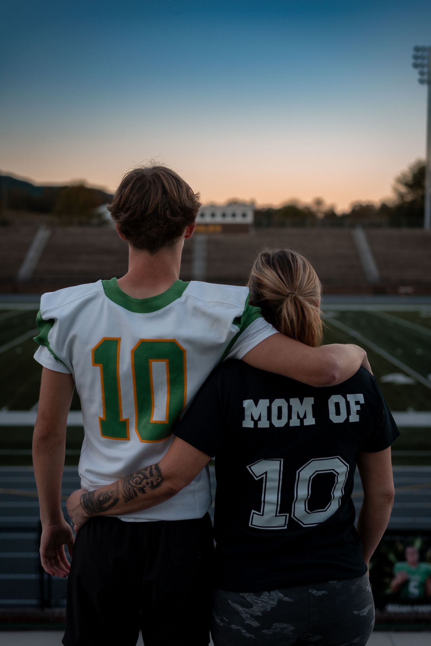 Football player and supporter stand together at sunset on an empty field.