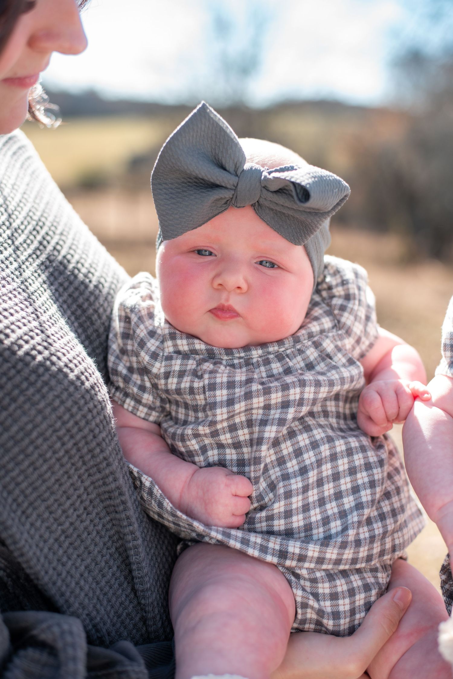 Baby wearing gingham outfit and cap photographed in natural sunlight.