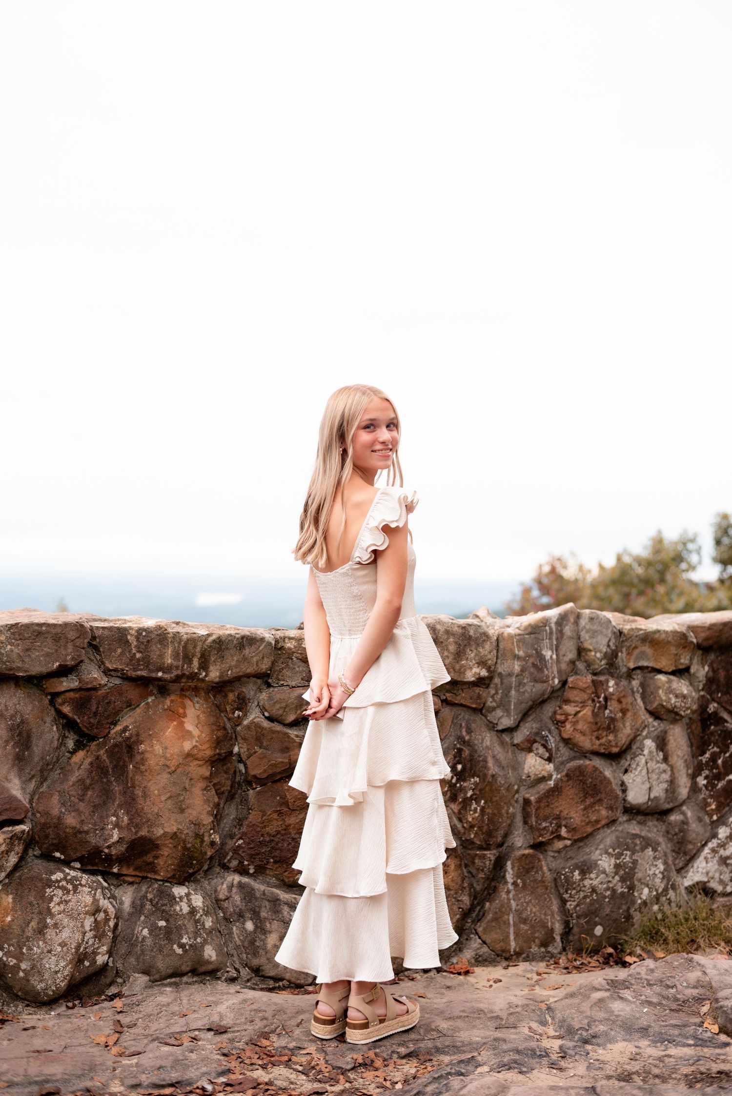 Cream colored ruffle dress photographed against rustic stone wall outdoors.
