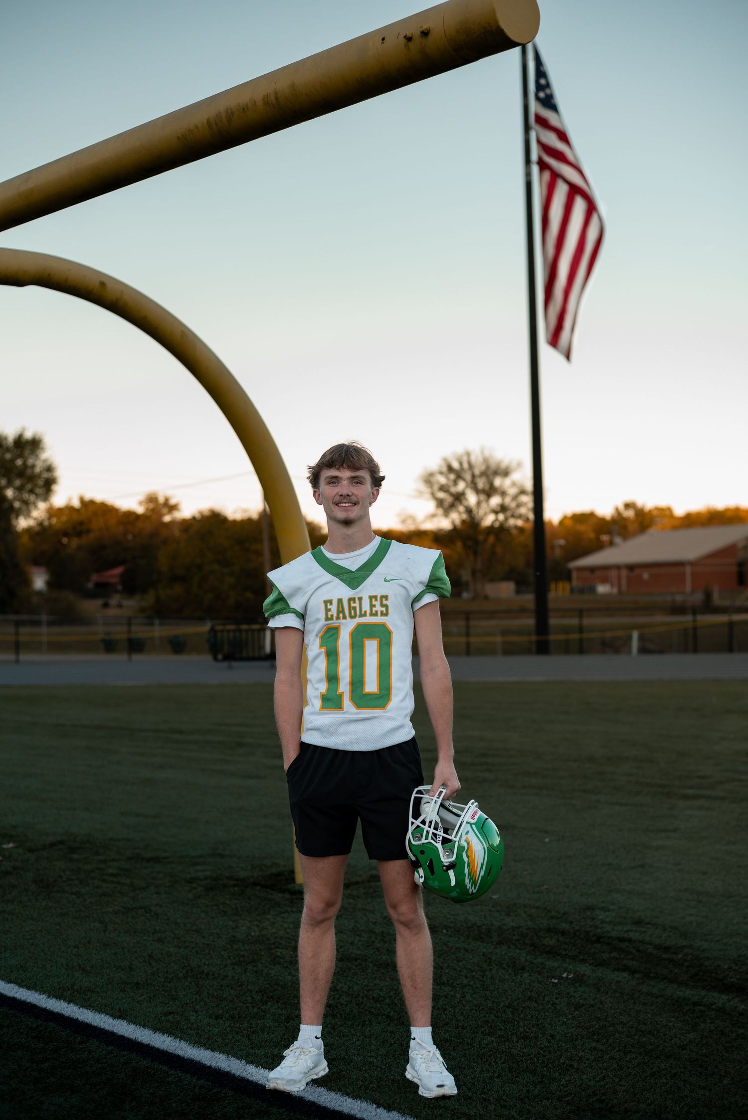 Football player stands under goal post with American flag waving in background.