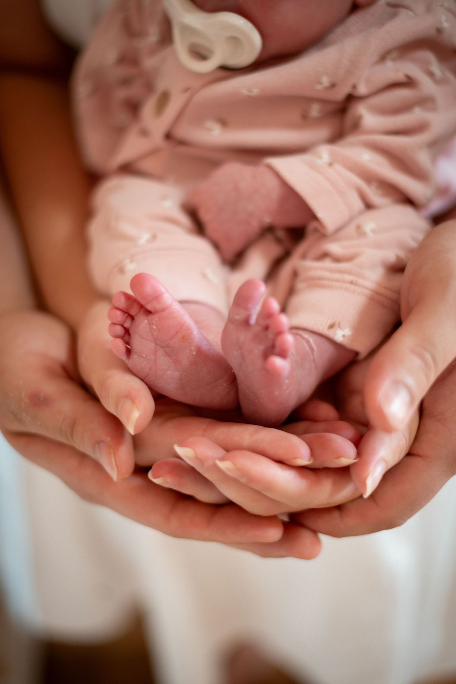 Close-up of tiny newborn feet being cradled in adult hands with soft lighting.