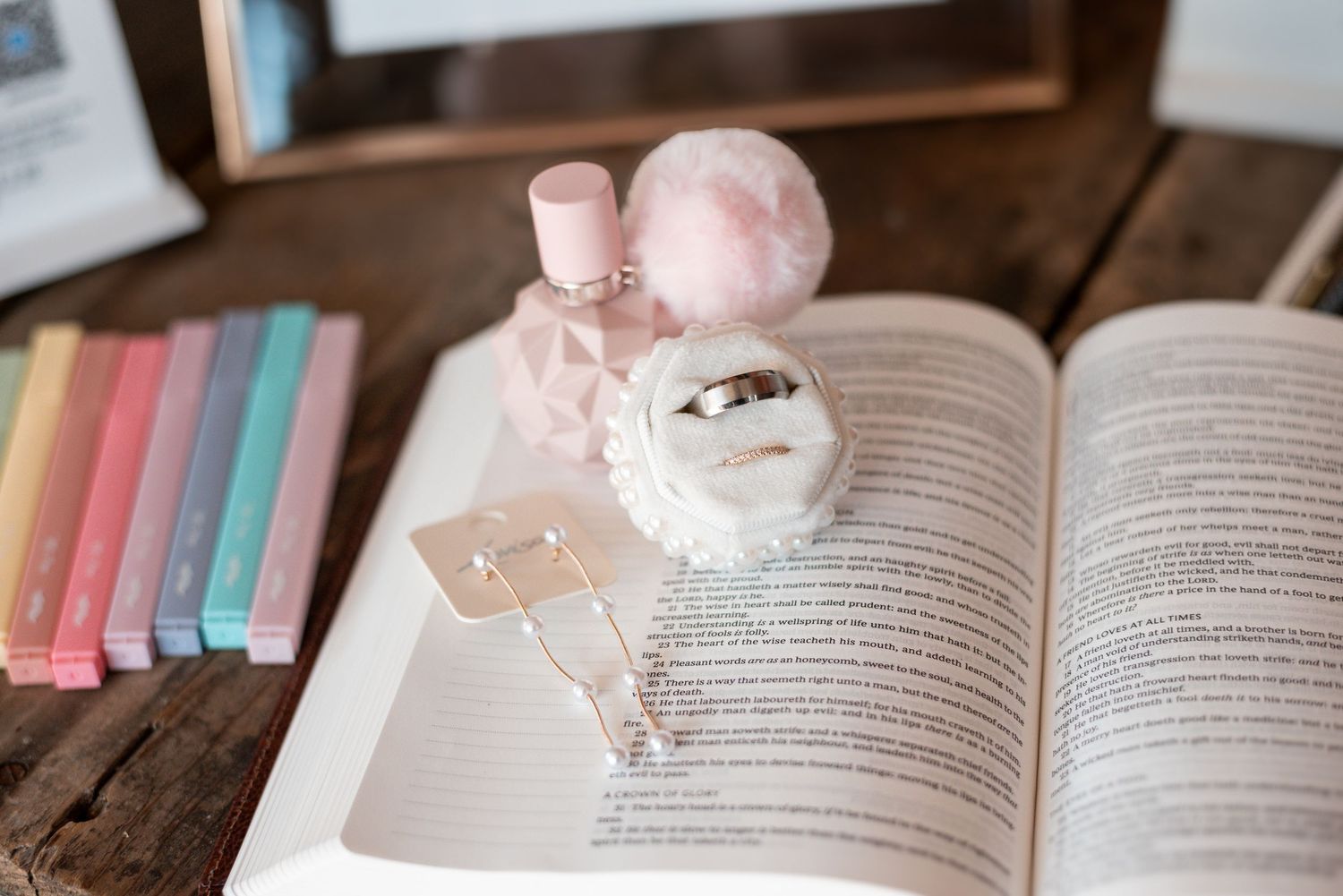 Pink and white decorative items arranged on an open book with colorful spines in background.