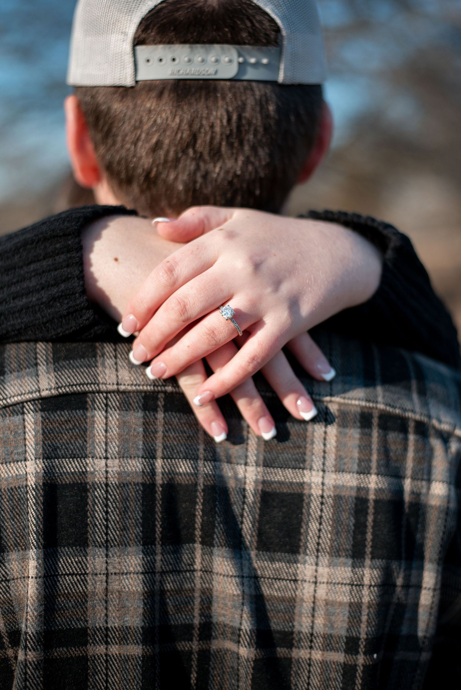 Close-up of hands displaying engagement ring while embracing in plaid shirt.