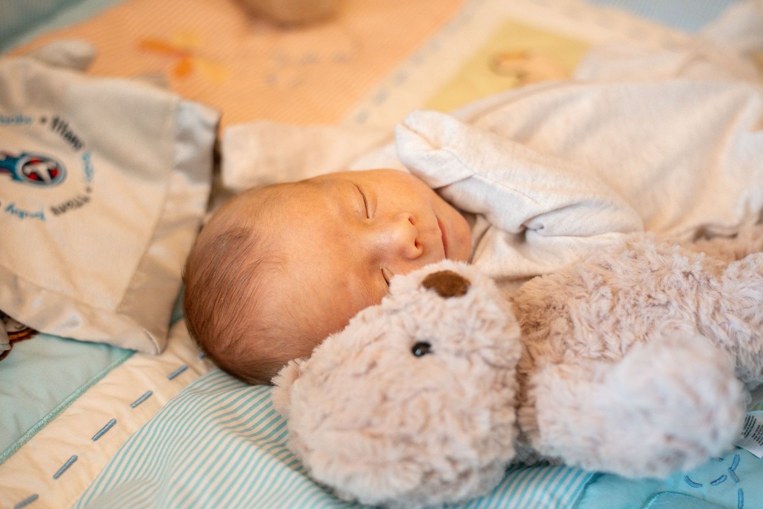 Newborn baby sleeps on light blue bedding in wooden crib.