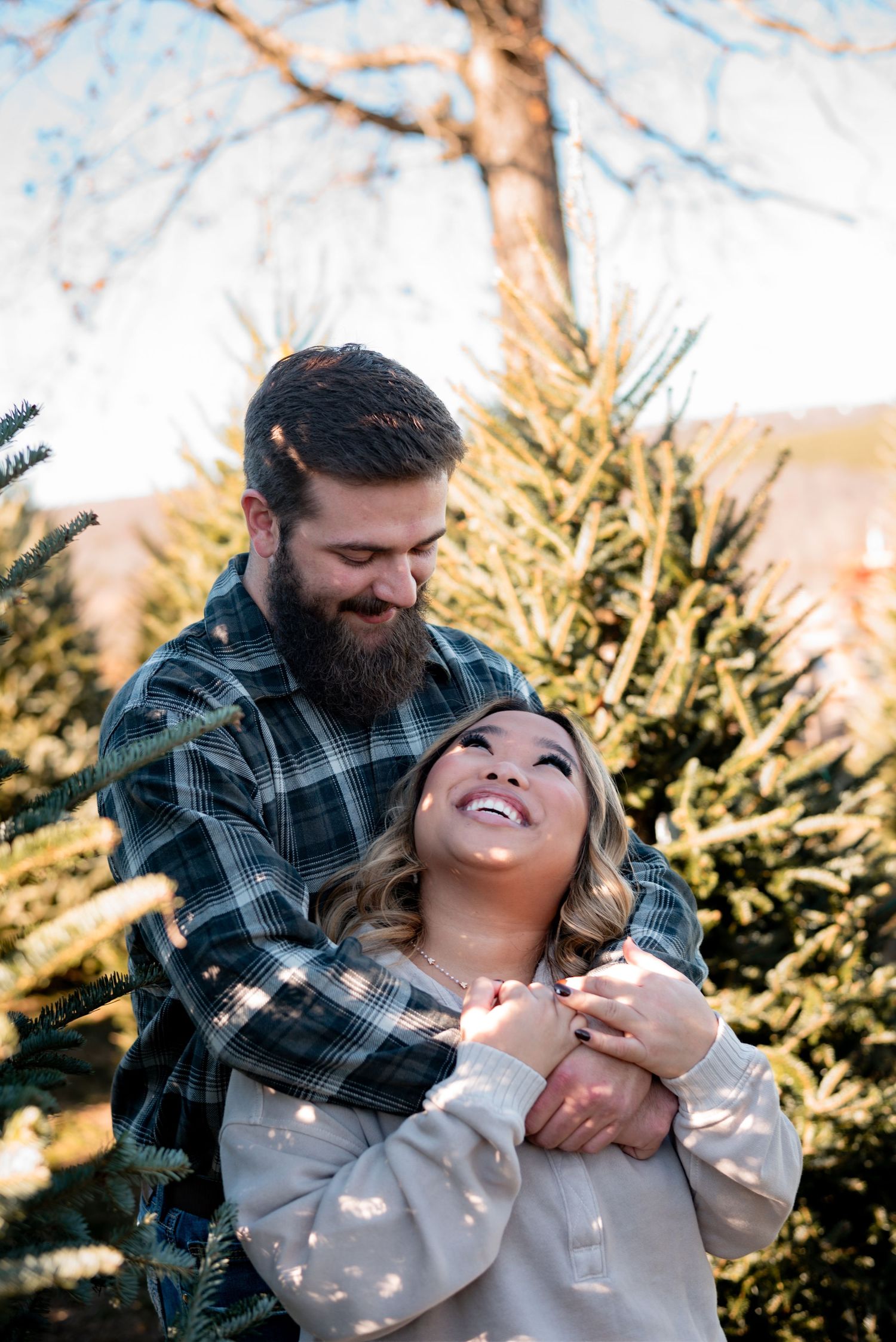 Playful couple laughing together during winter photoshoot at Christmas tree farm.