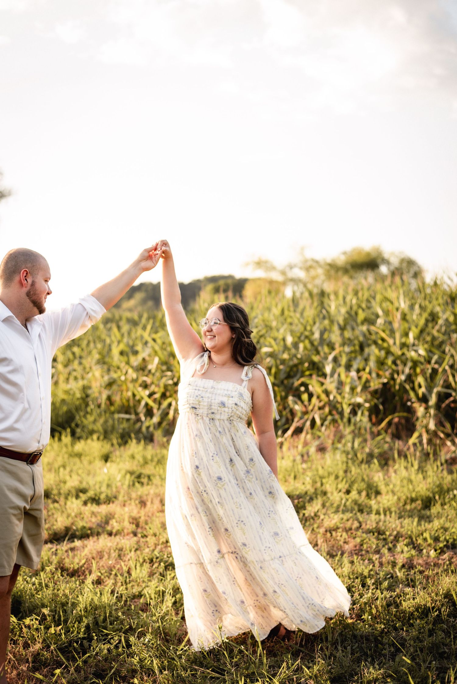 Couple dancing and twirling in a sunlit field wearing white.