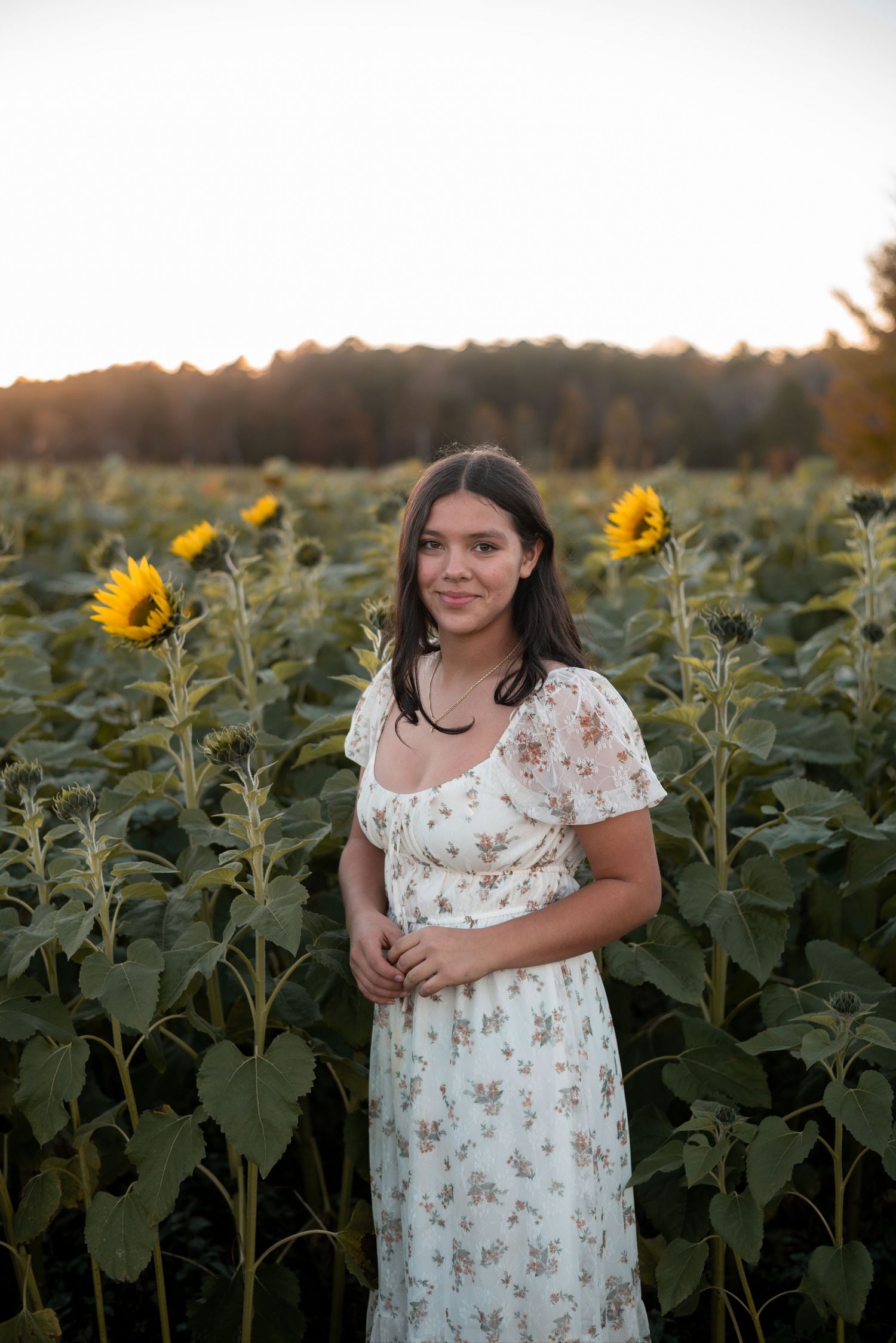 Person in floral dress poses in a sunflower field during golden hour.