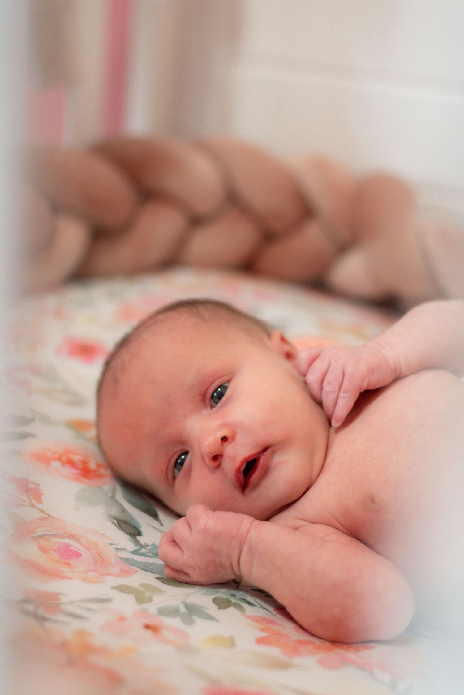 Newborn baby lying on floral bedding looking at camera with peaceful expression.