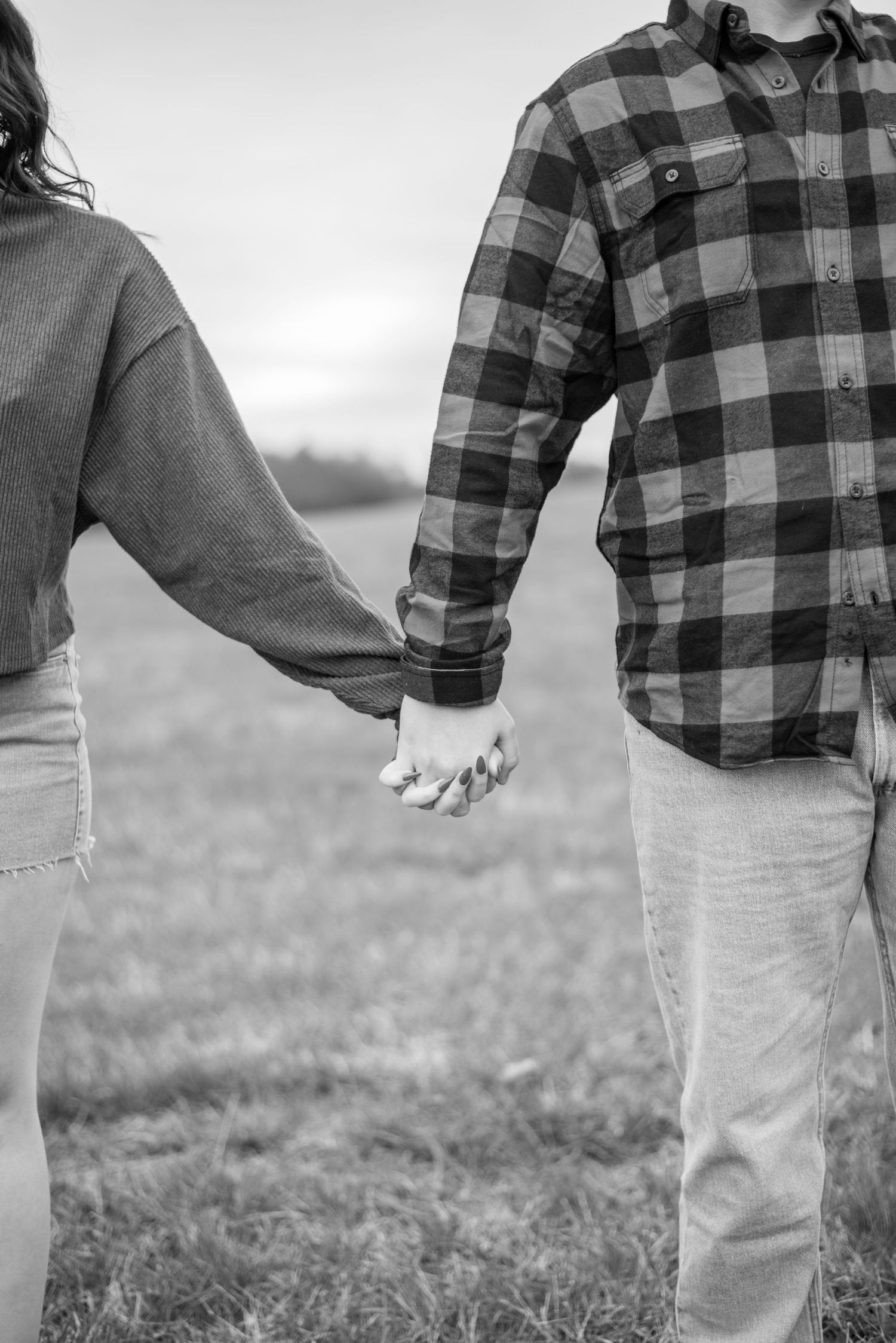 Black and white image of couple holding hands while walking, showing plaid shirt and jeans.
