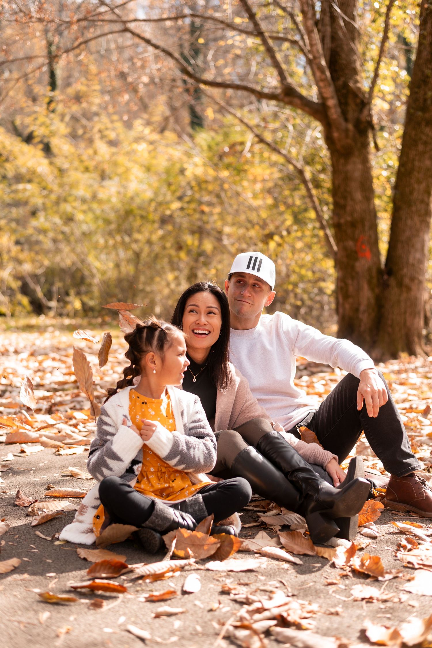 A family sits together on fallen autumn leaves enjoying a casual outdoor moment.