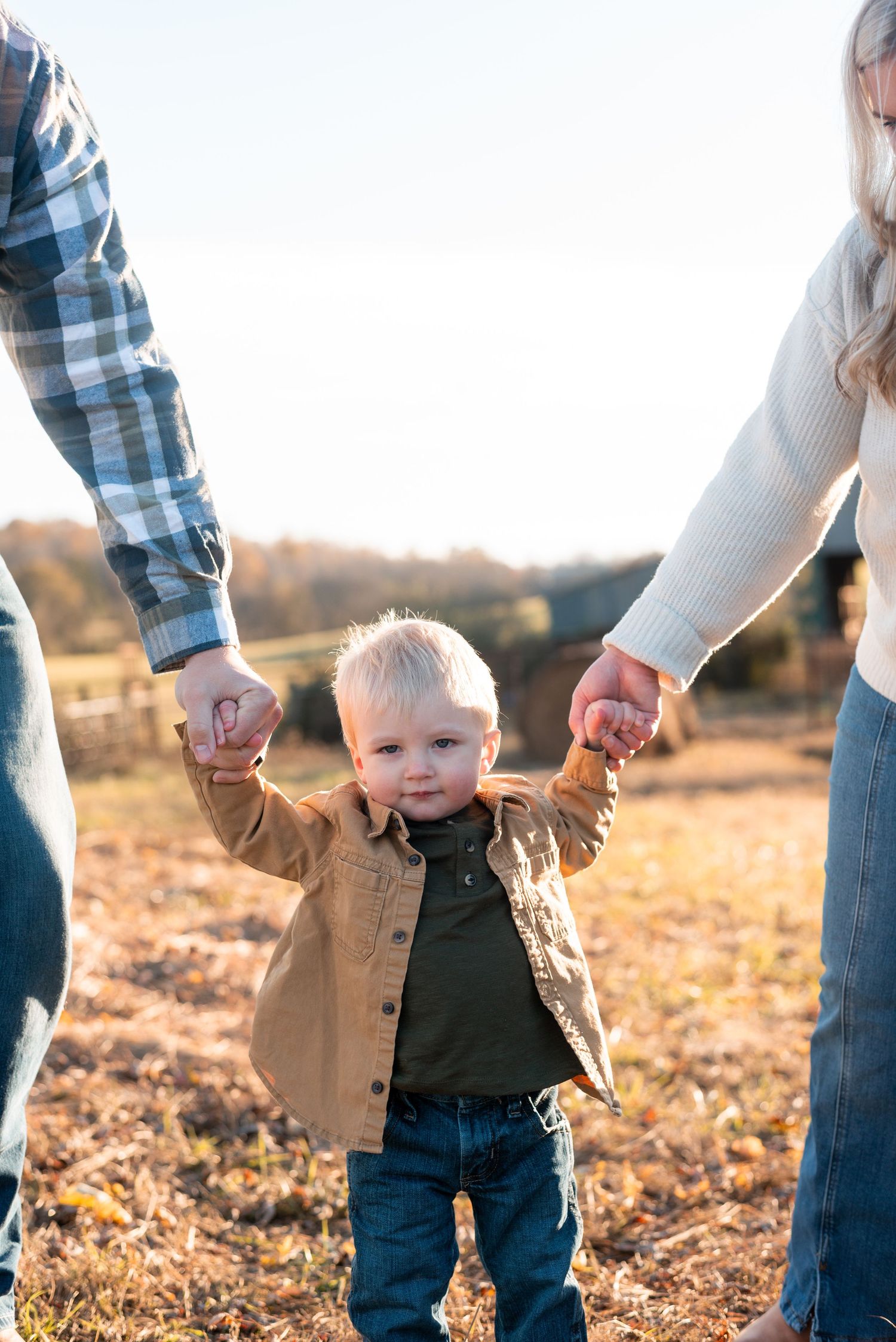 Small child walks hand in hand with parents during sunset in a field.