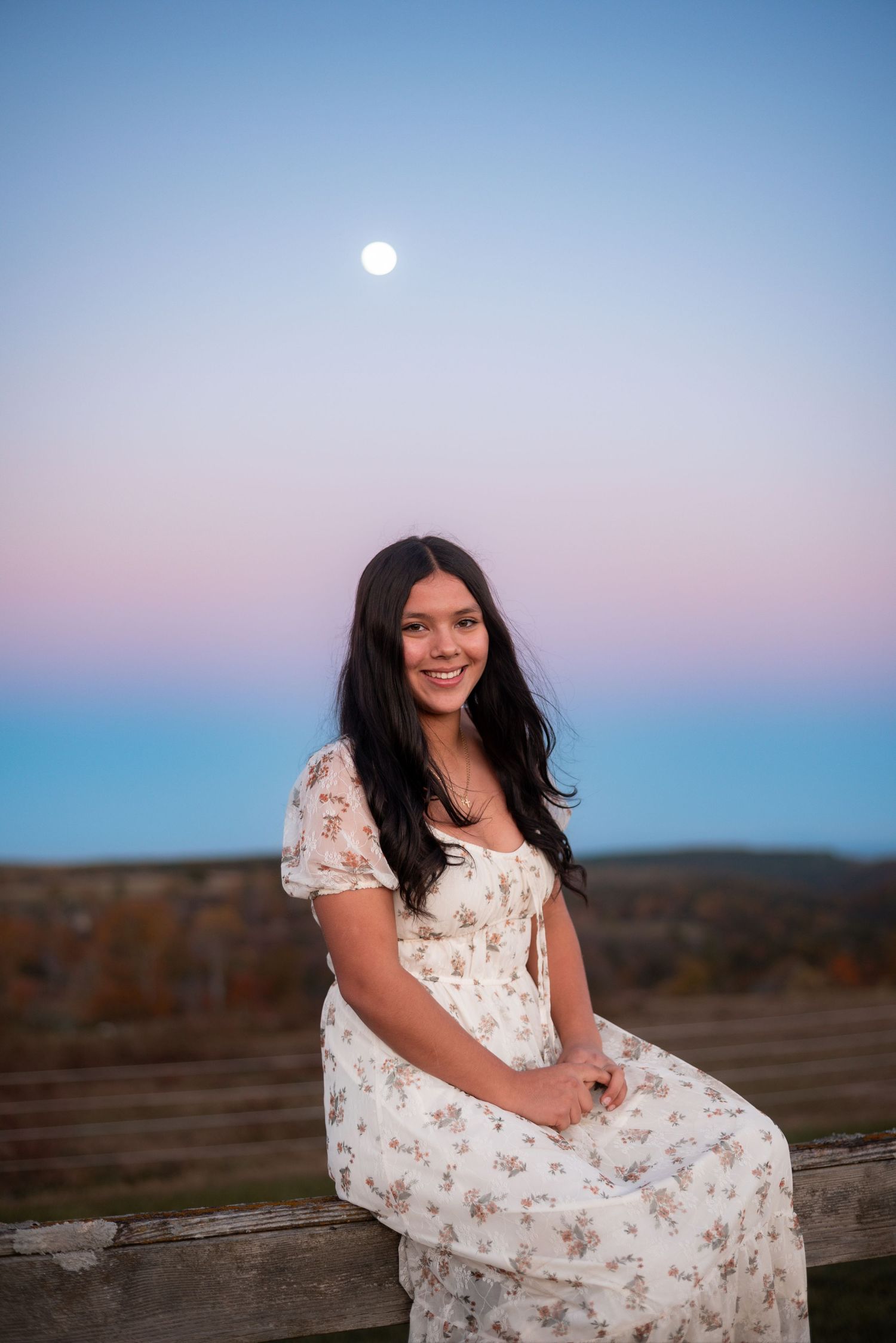 A floral white dress flows in the evening breeze as the moon rises over a desert landscape.