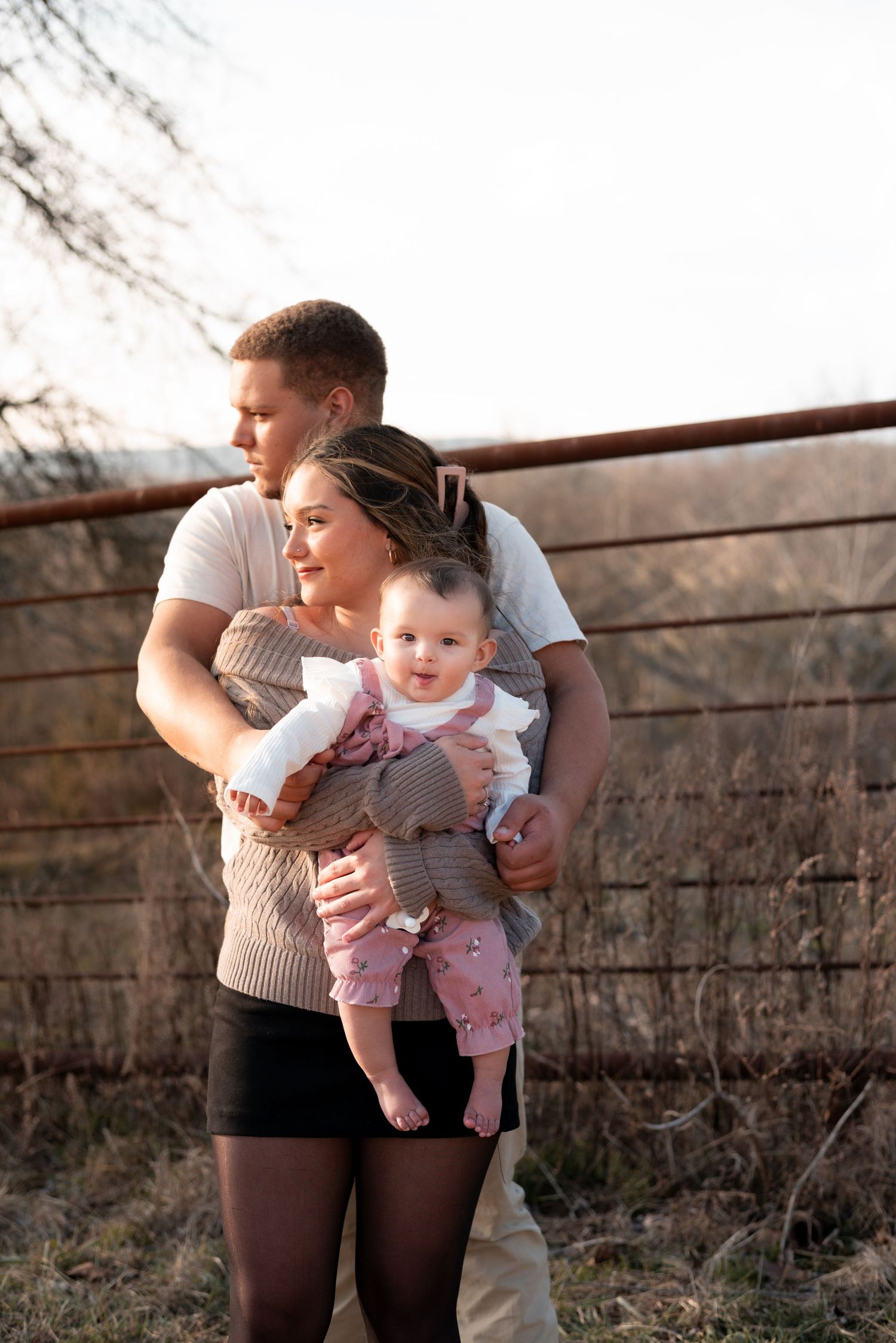 Family group posing together by rustic fence during golden hour.