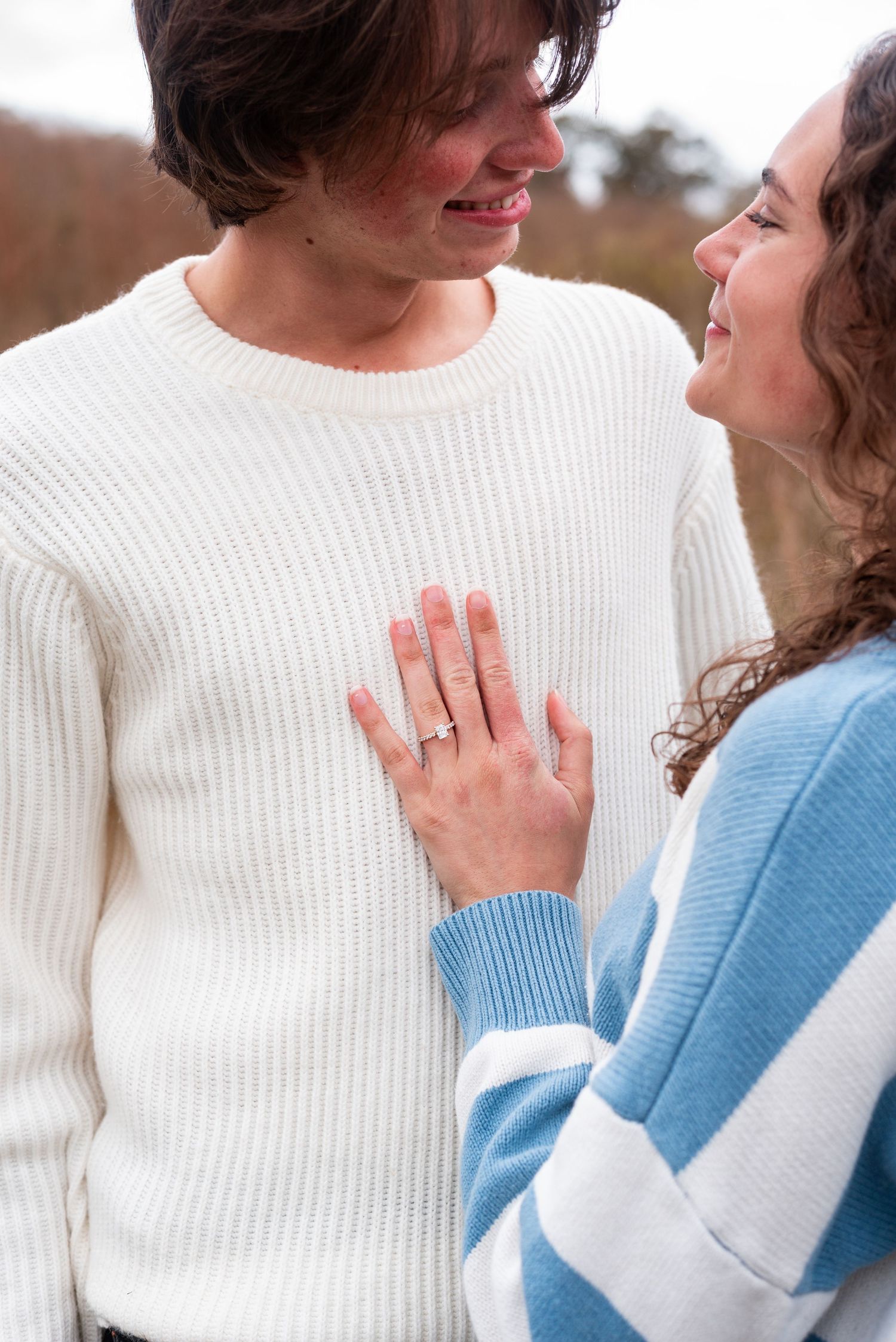 Engagement photos showing couple in white and blue sweaters displaying ring.