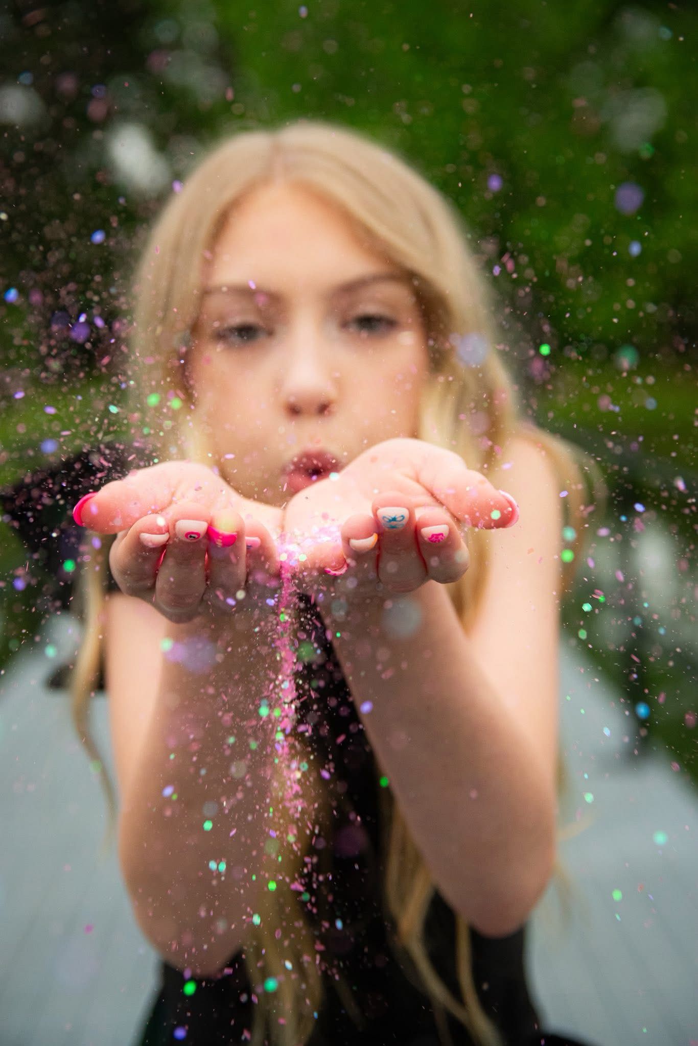 Person blowing sparkly glitter from cupped hands with magical effect.