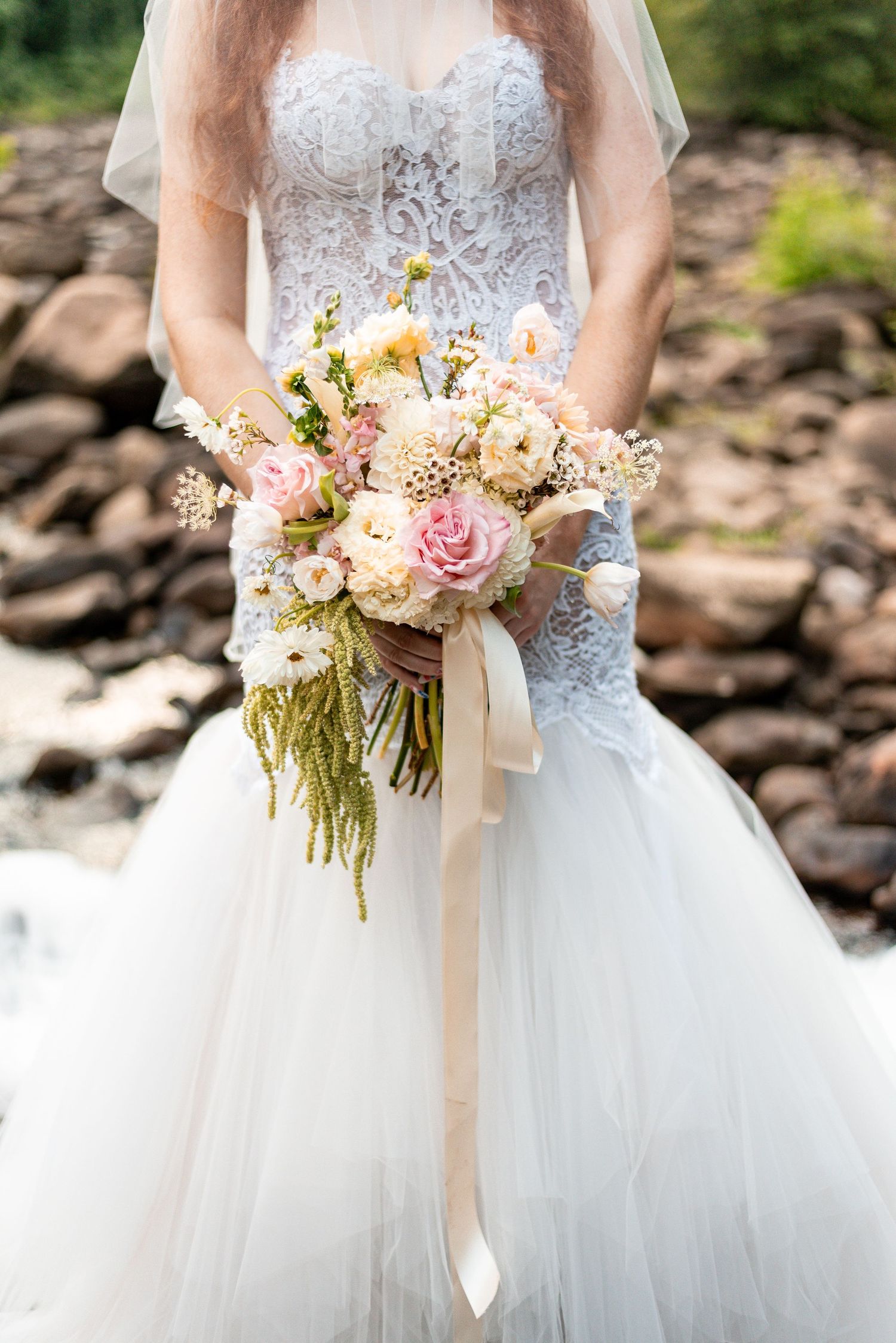 Bride in lace mermaid gown holding romantic blush and cream wedding bouquet with trailing ribbon.
