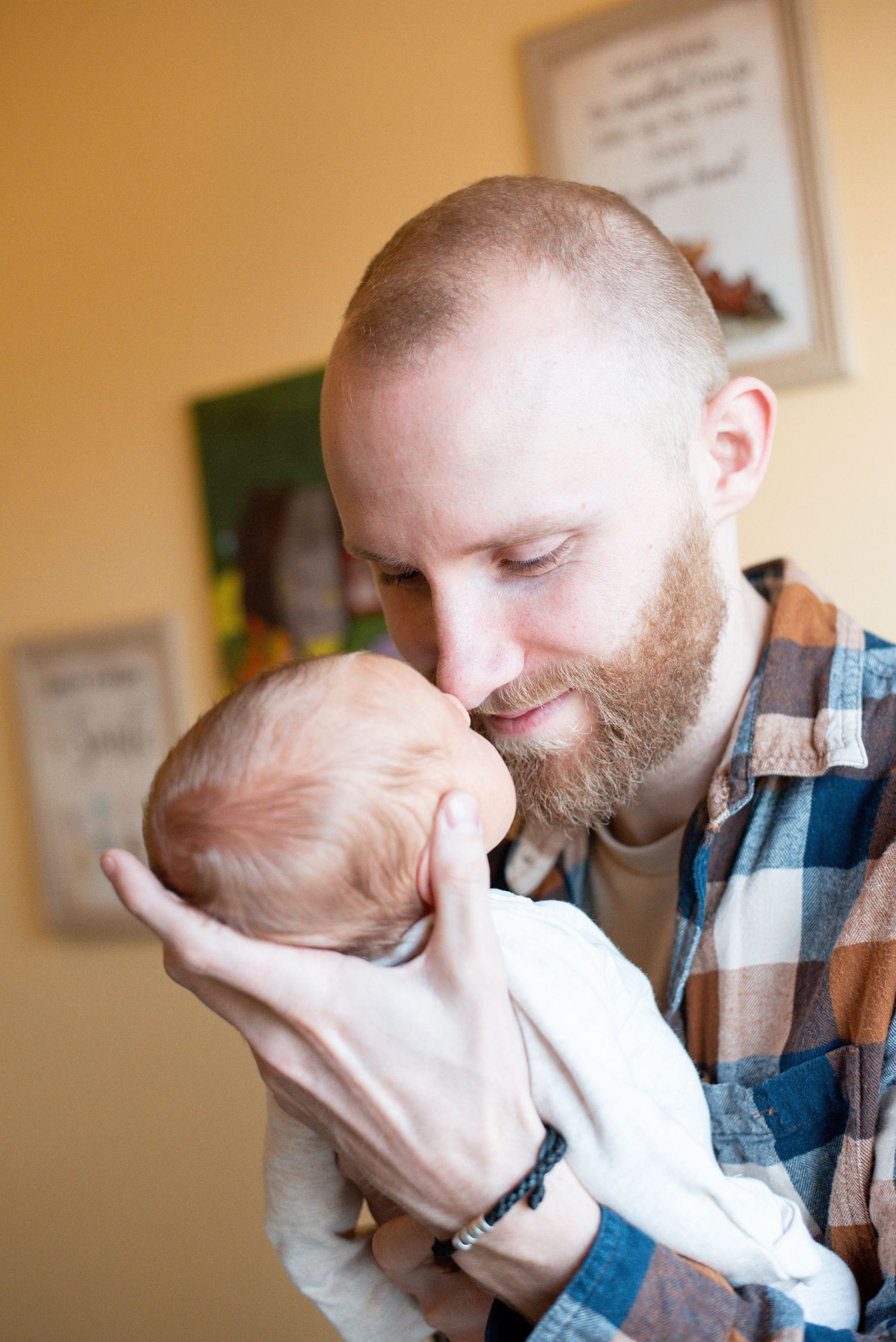Father holds and kisses newborn baby in emotional indoor portrait series.