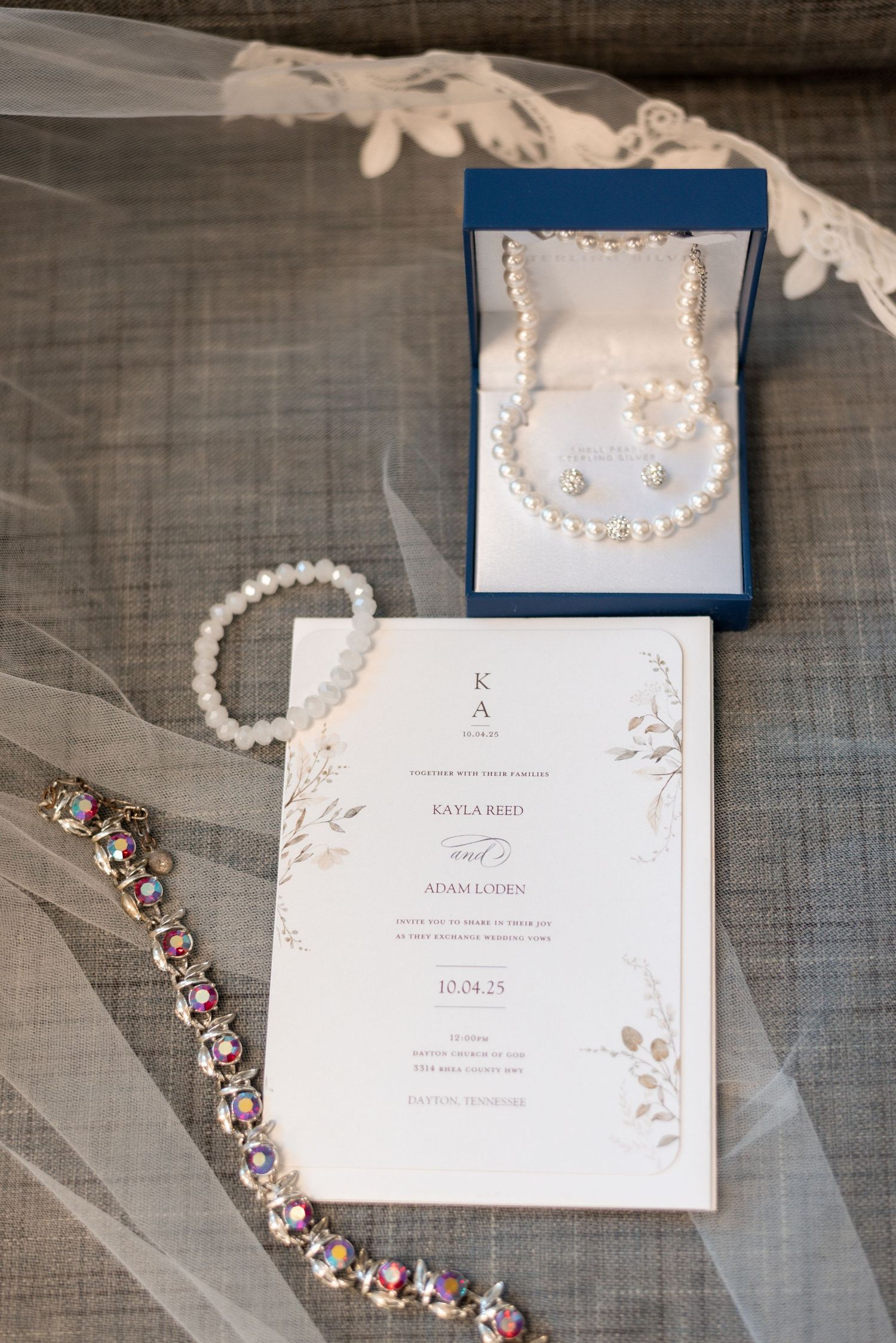 Elegant wedding invitation suite with pearl necklace and jewelry on gray linen background.