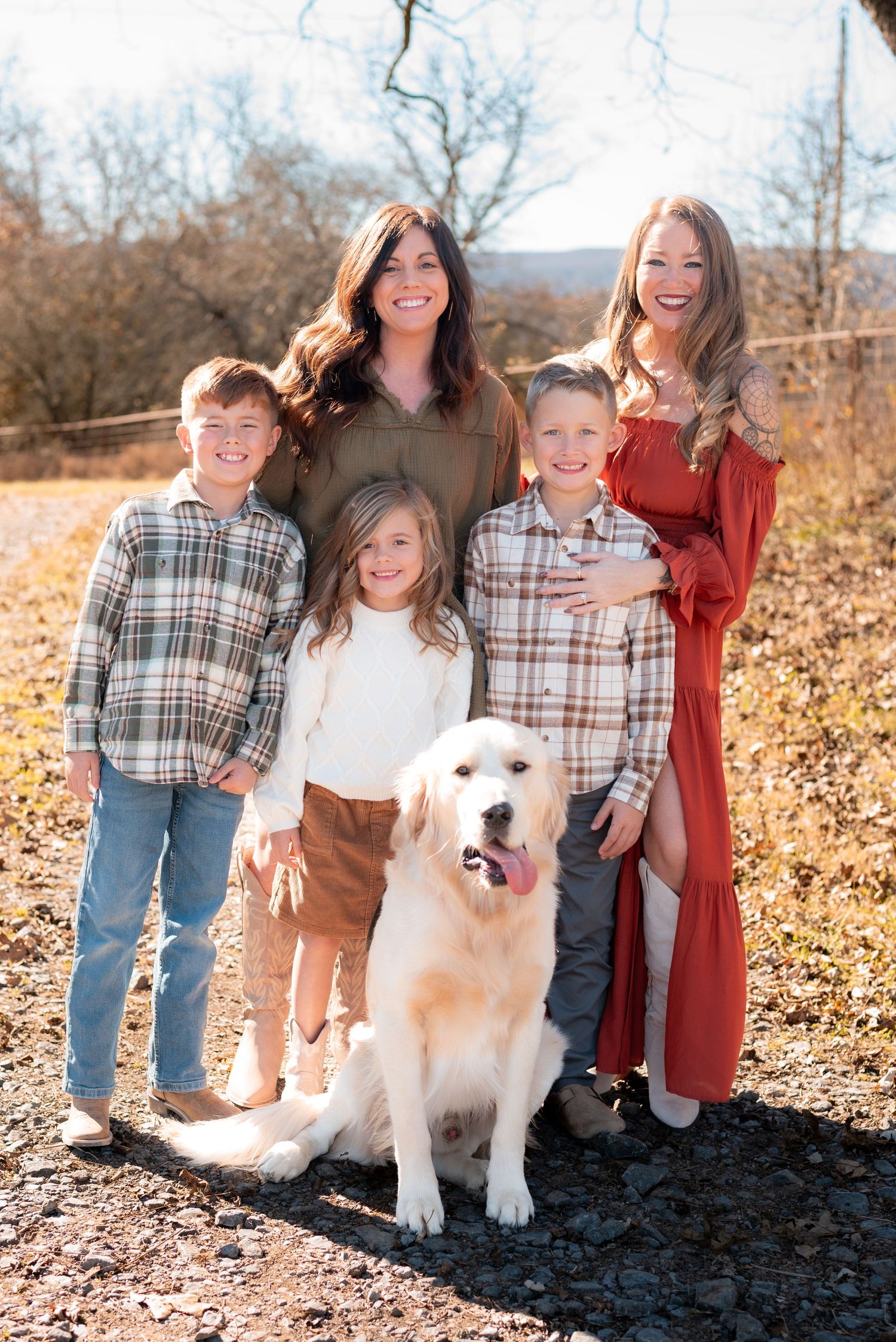 Family portrait with white dog in autumn setting with fallen leaves.