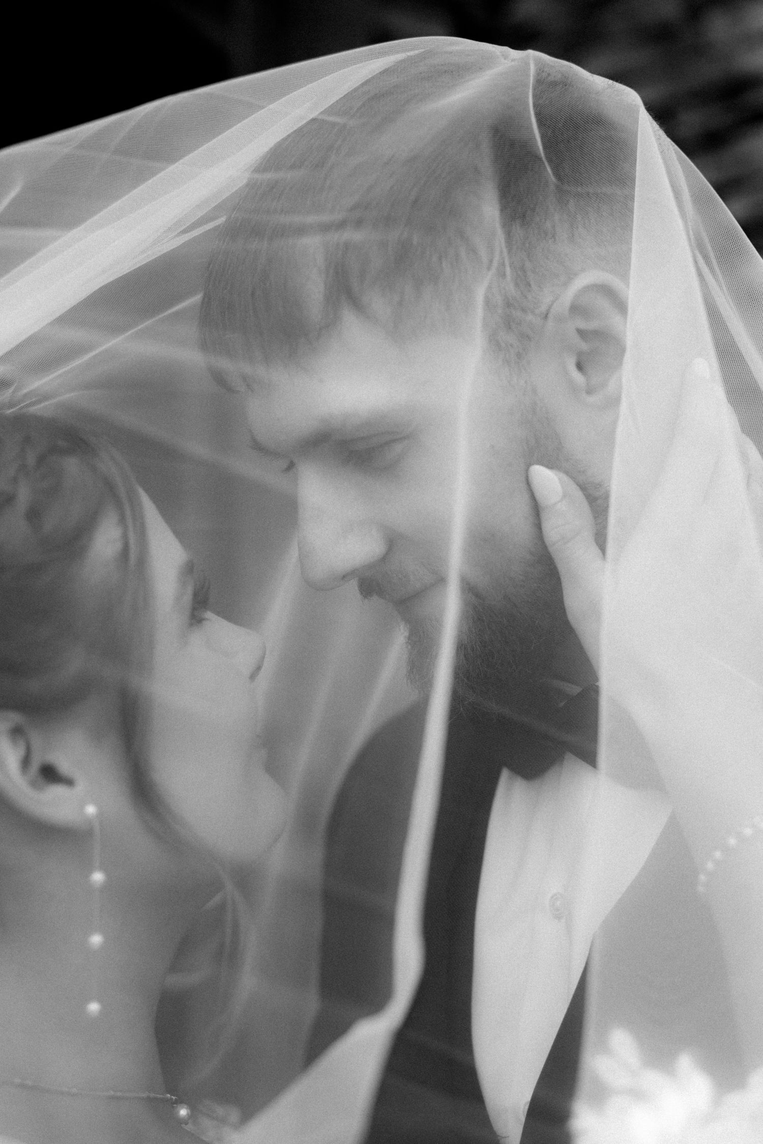 An intimate black and white portrait of a couple beneath a delicate veil.
