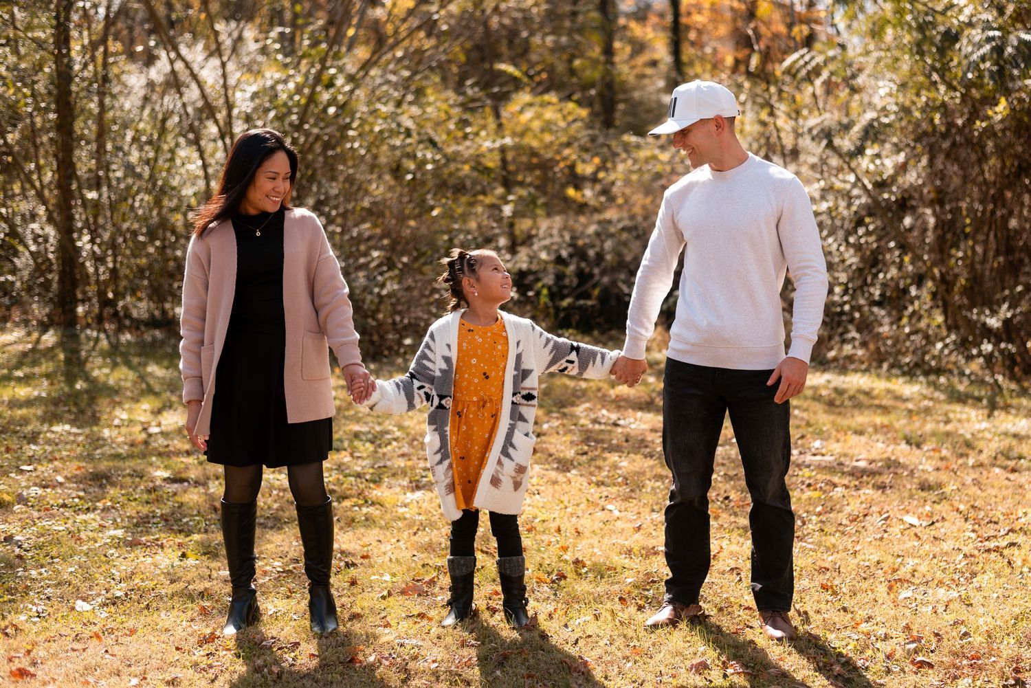 A family walks together through a sunlit autumn forest path.