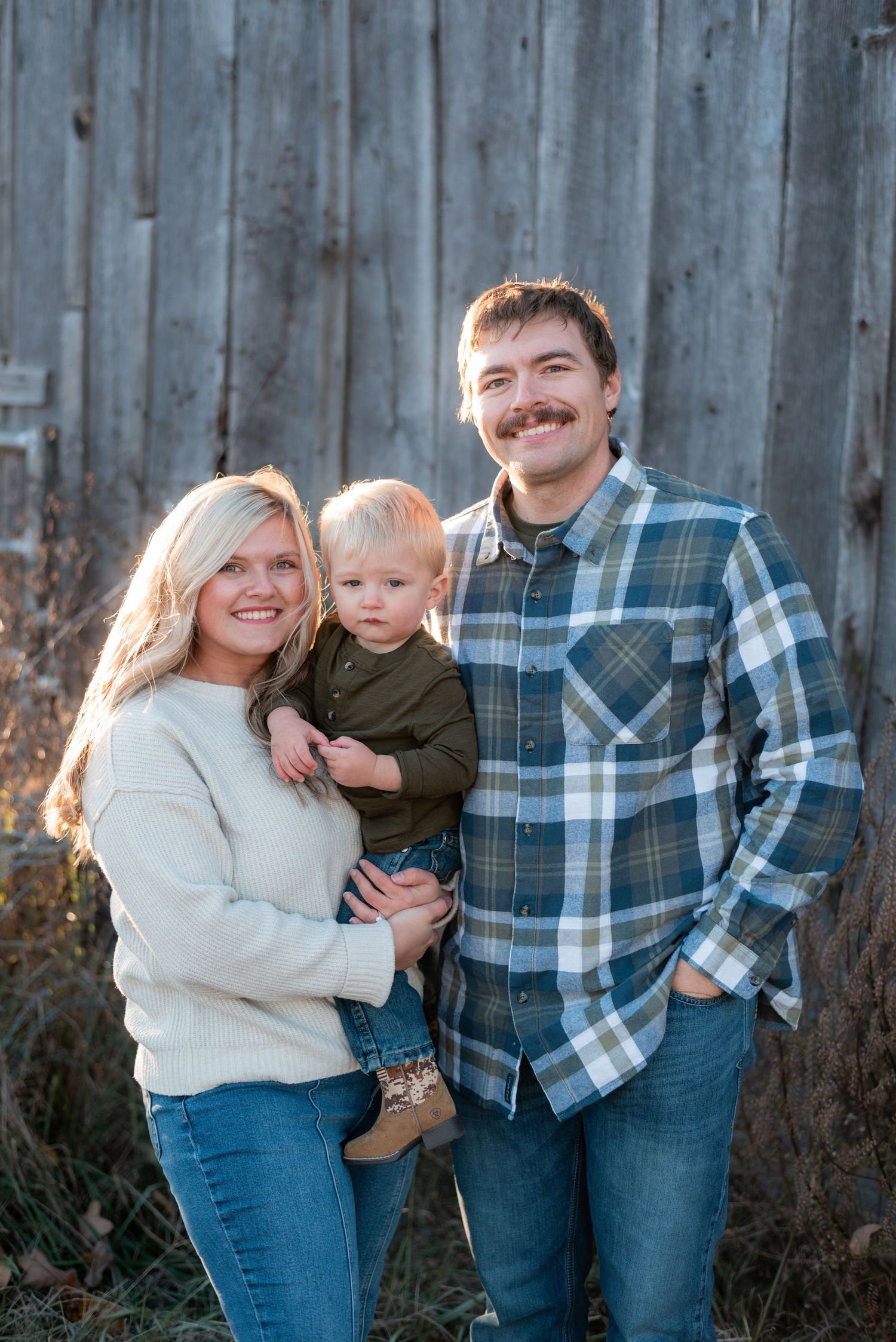 Family poses together against rustic wooden fence during outdoor photo session.
