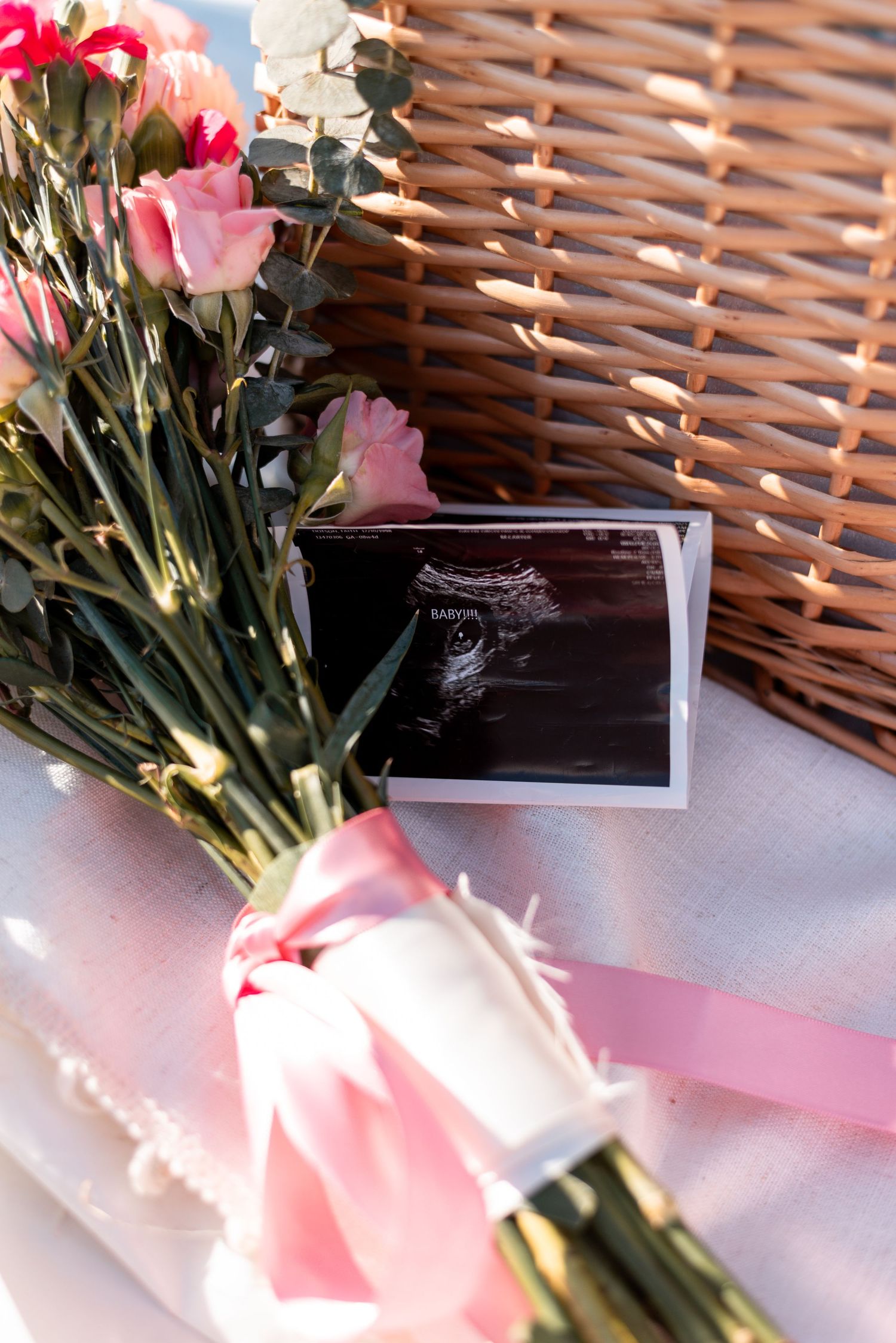 Pink roses and a small card arranged with pink ribbon near wicker basket edge.