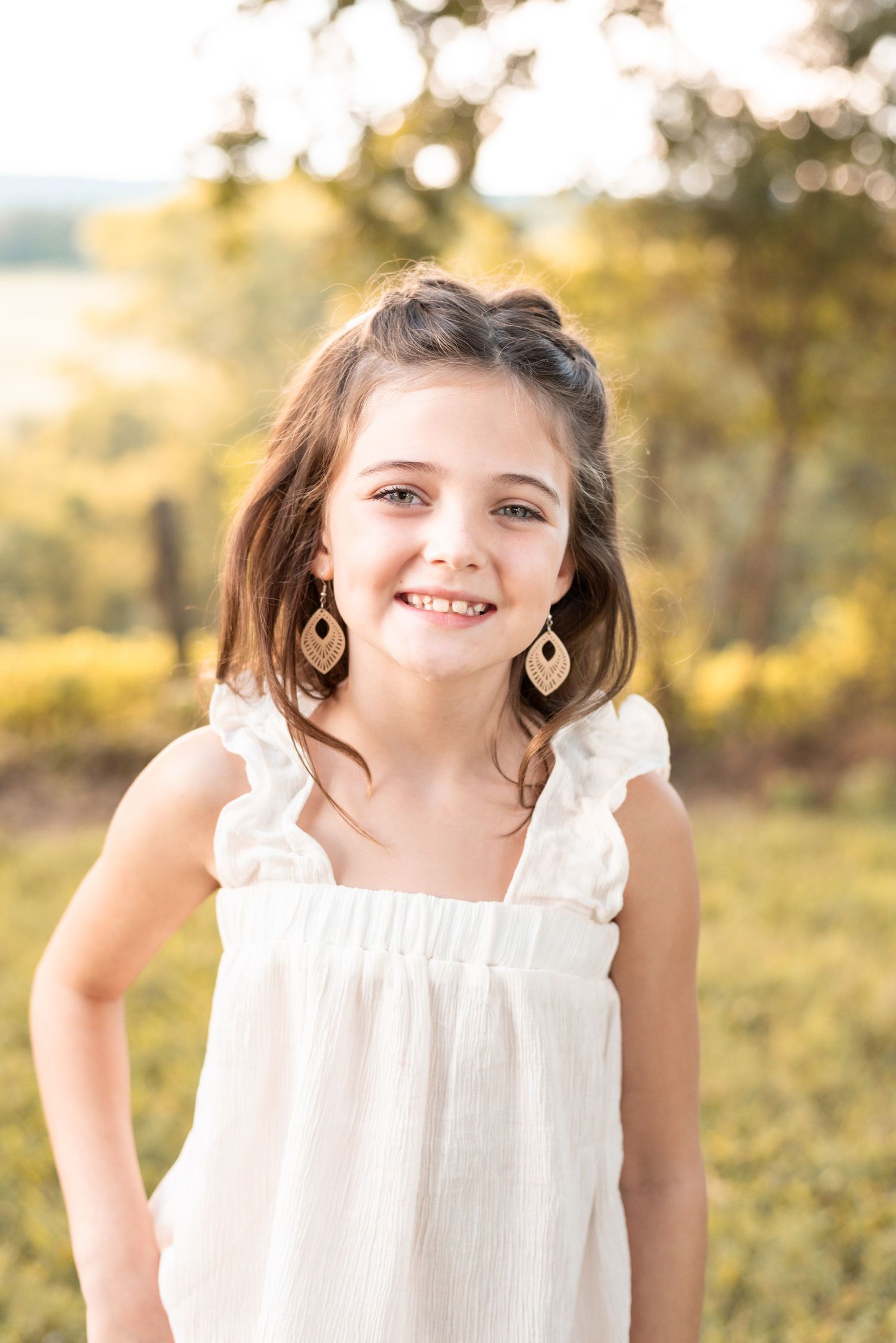 Young girl in white dress smiles during outdoor summer photoshoot.