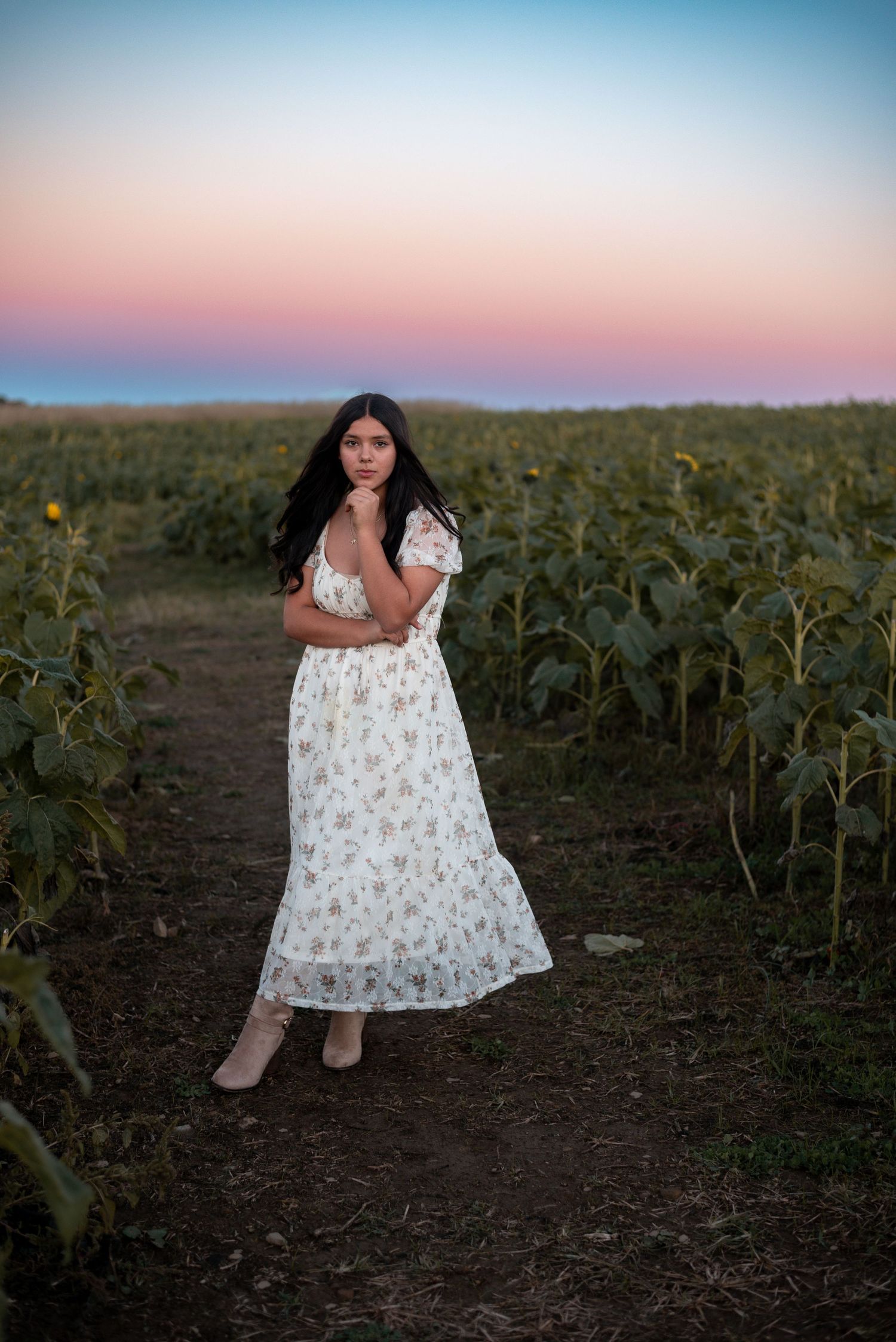 Full length portrait in floral dress walking through sunflower field at dusk.
