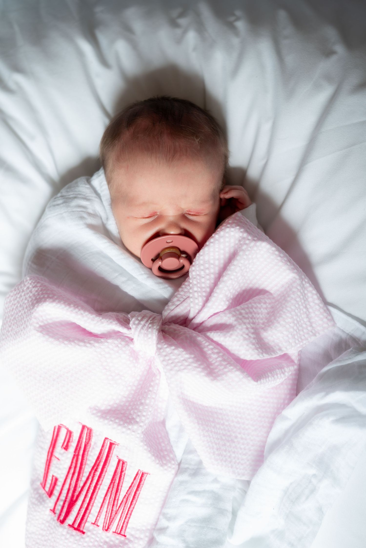 Baby wrapped in white textured blanket with monogram sleeping peacefully.