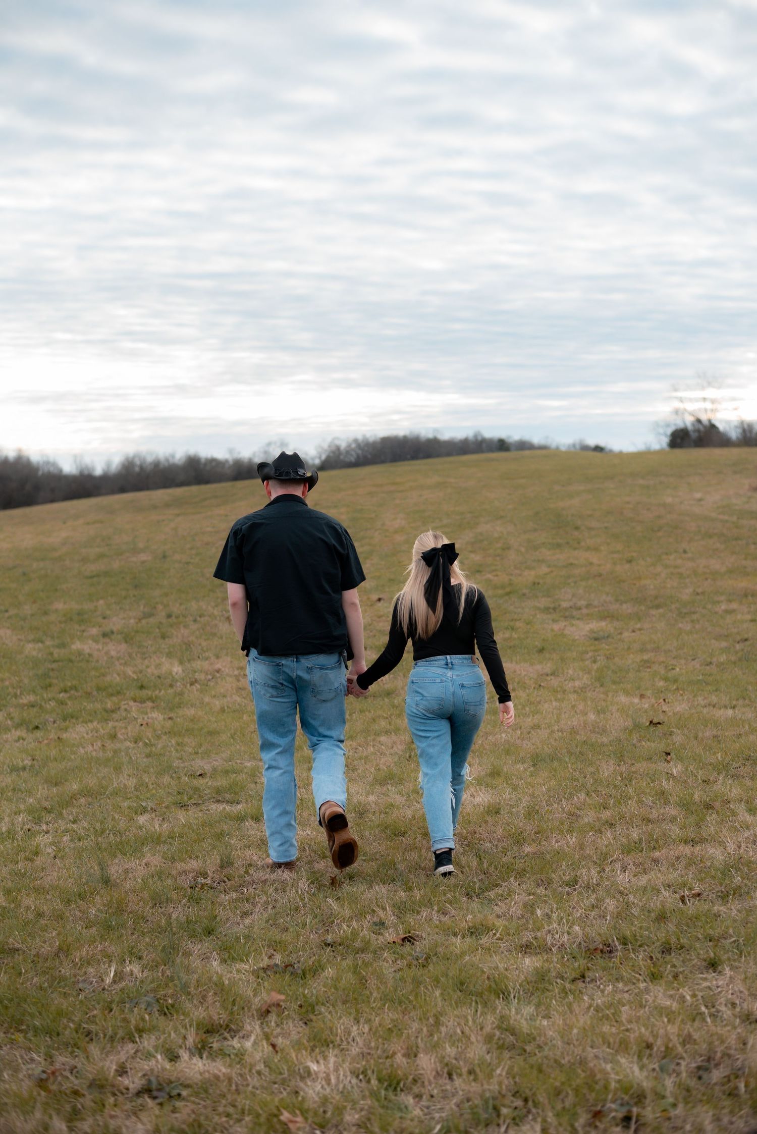 Two people walking hand in hand across a scenic hilltop meadow.